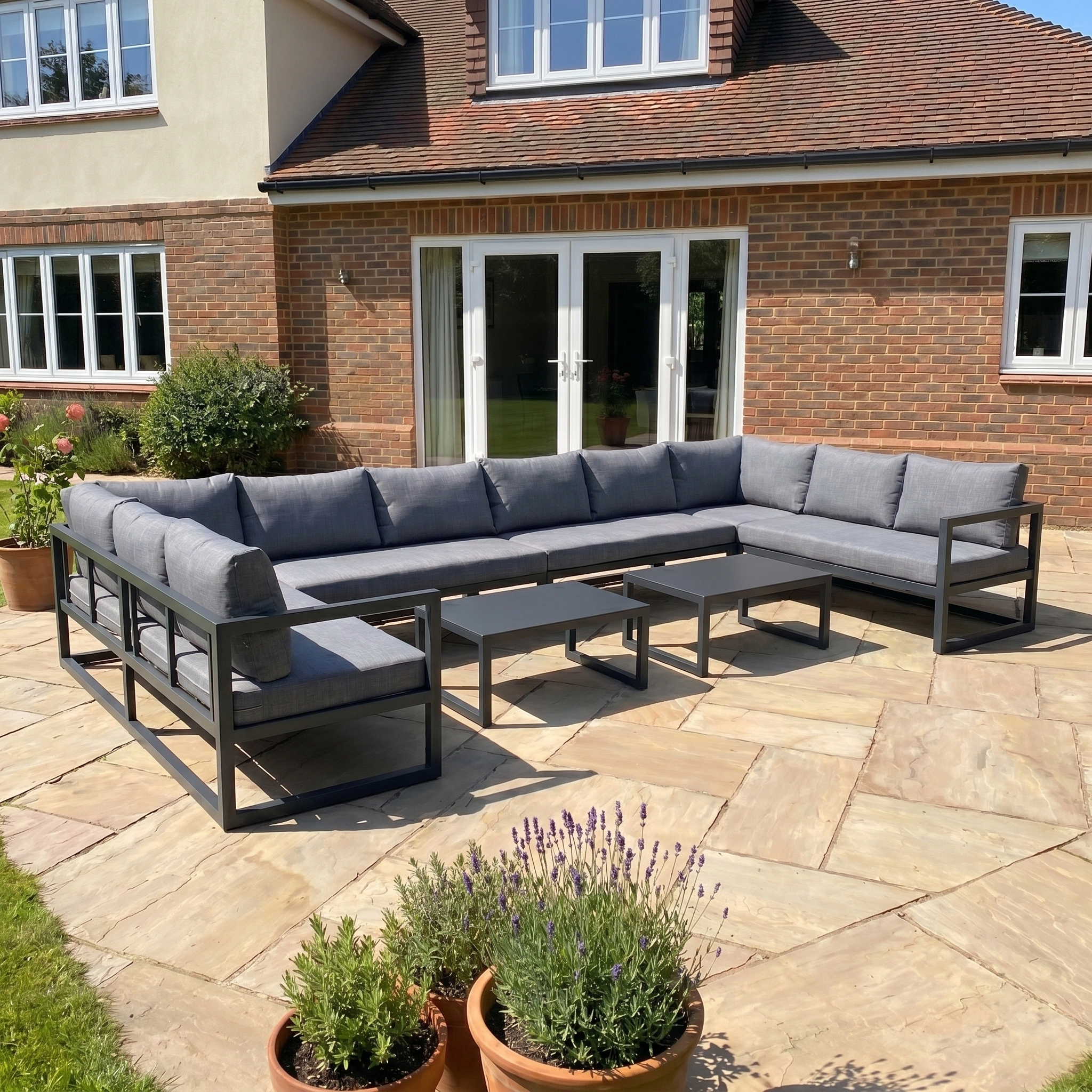 The Havana U-Shape Corner Group Set with Reclining Feature and Coffee Tables in Charcoal offers stylish comfort on a stone patio outside a brick house, perfect for relaxing outdoors.