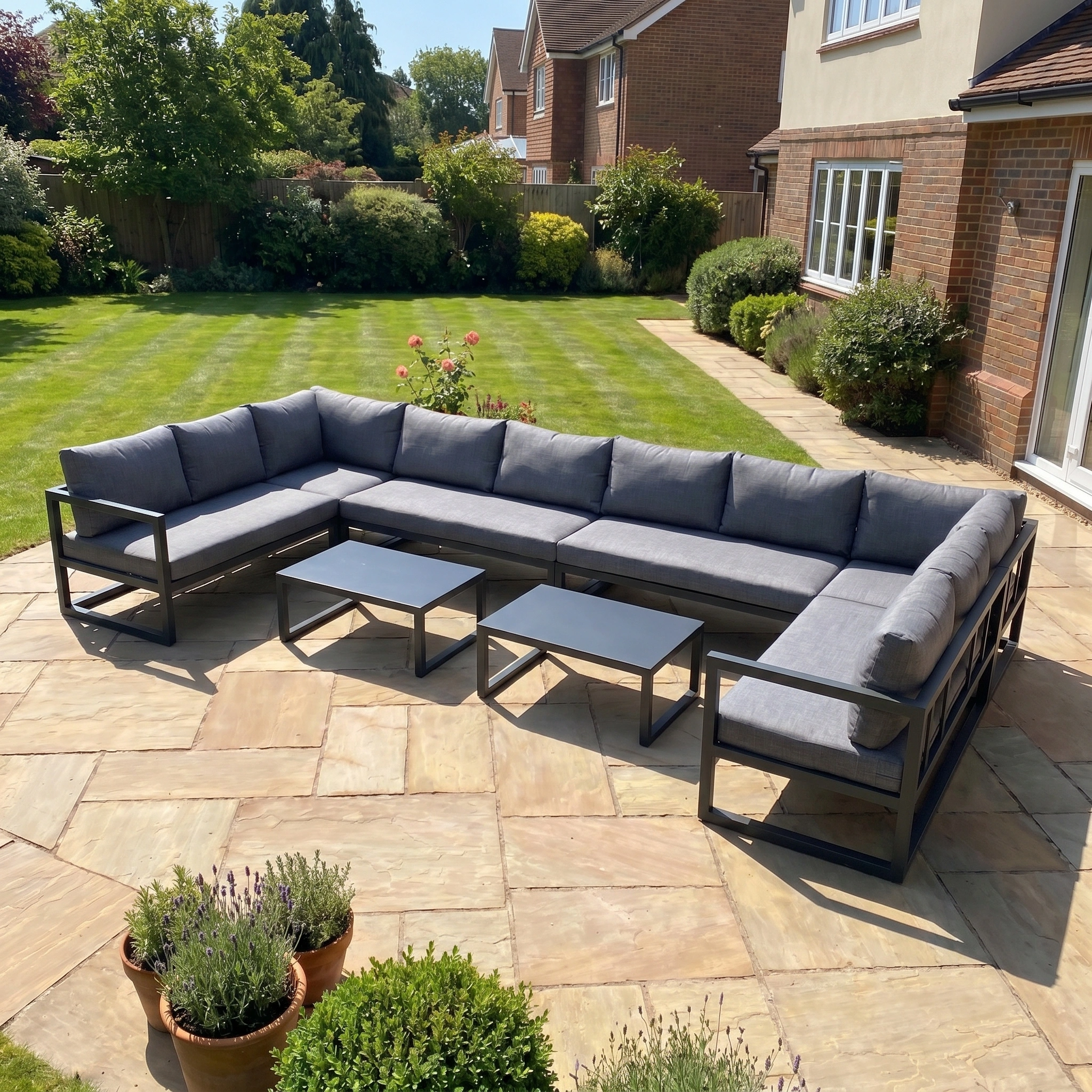 The Havana U-Shape Corner Group Set with Reclining Feature and Coffee Tables in Charcoal sits on a stone patio in a sunny, well-kept garden.