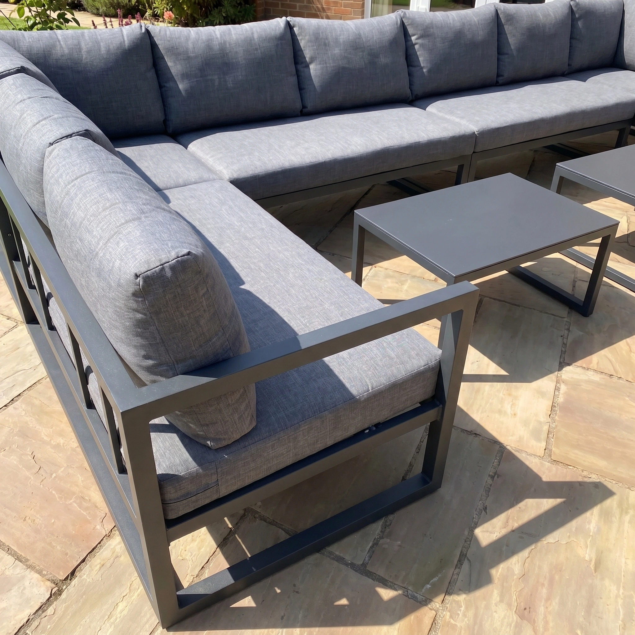 The Havana U-Shape Corner Group Set with Reclining Feature and Coffee Tables in Charcoal brings comfort and elegance to your garden retreat, perfect for relaxing outdoors on a stone patio in the sunlight.