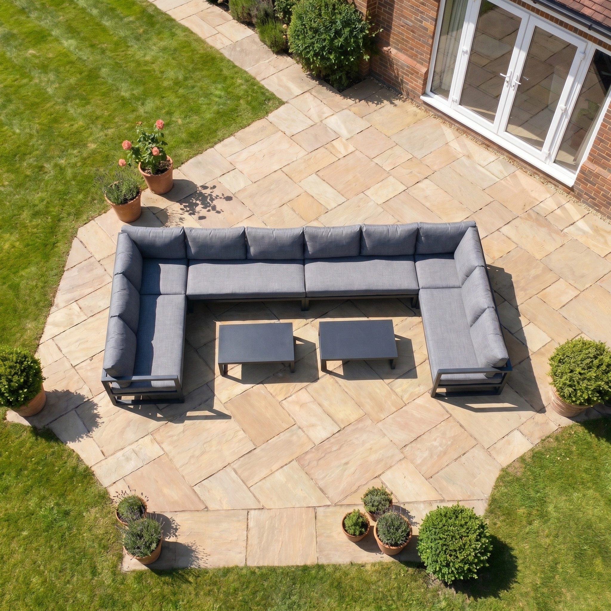Aerial view of the Havana U-Shape Corner Group Set with Reclining Feature and Coffee Tables in Charcoal, arranged on a sandstone patio surrounded by grass.