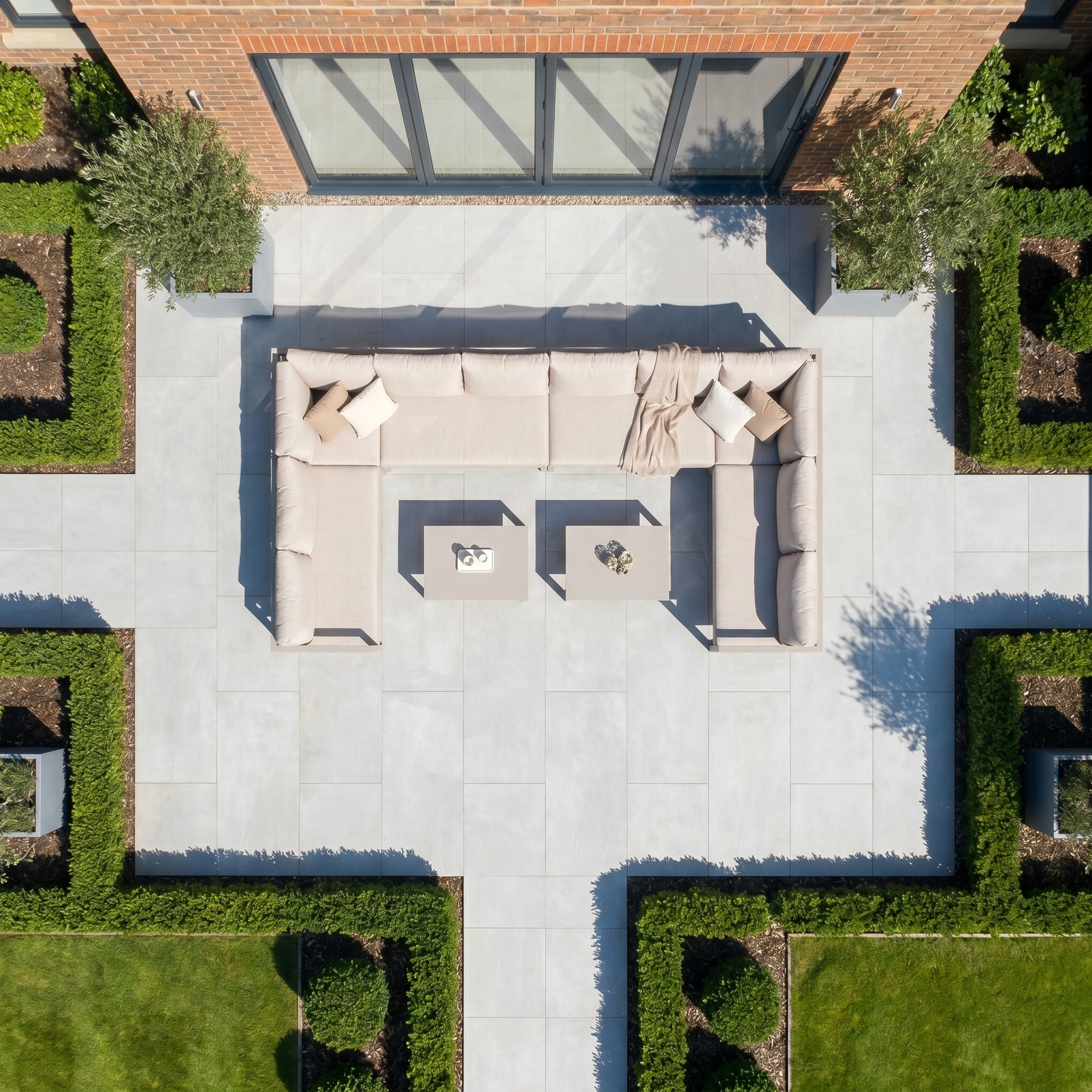 Aerial view of a modern patio featuring the Havana U-Shape Corner Group Set with Reclining Feature in Latte, two coffee tables, UV-resistant cushions, and surrounding manicured hedges.
