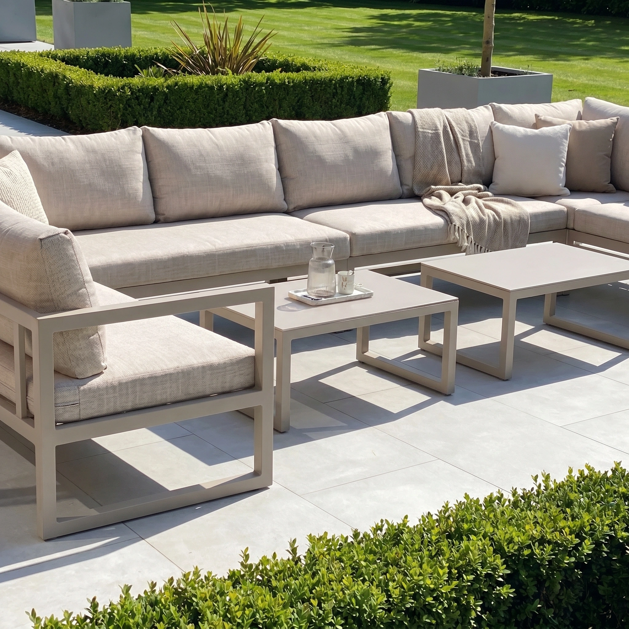 The Havana U-Shape Corner Group Set in Latte, with reclining feature and coffee tables, offers stylish comfort for relaxing outdoors on your patio, surrounded by greenery.