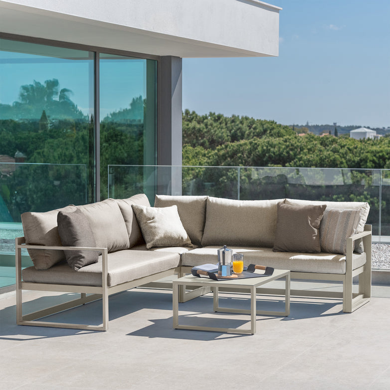 Outdoor patio featuring the Havana Corner Group Set with Reclining Feature and Coffee Table in Latte—ideal for relaxing outdoors with a comfortable sectional and stylish table, all set against a scenic view through glass railings.