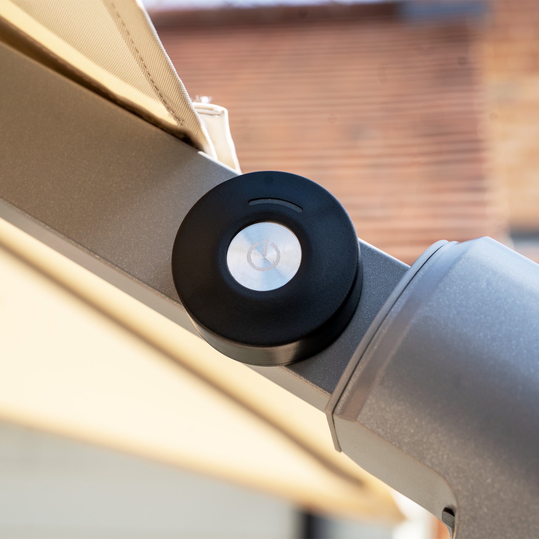 Close-up of a retractable awning mechanism featuring a sleek black circular casing and power button, complemented by LED lights for evening ambiance. The design is similar to the Hera 2.7m Square Cantilever Parasol with LED Lighting in Beige, merging functionality with style.