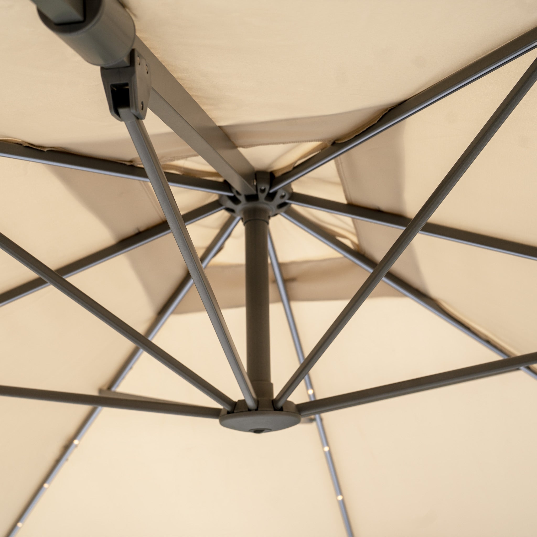 Close-up of the underside of an opened beige 2.7m Hera square cantilever parasol with LED lighting, highlighting metal spokes and central pole.