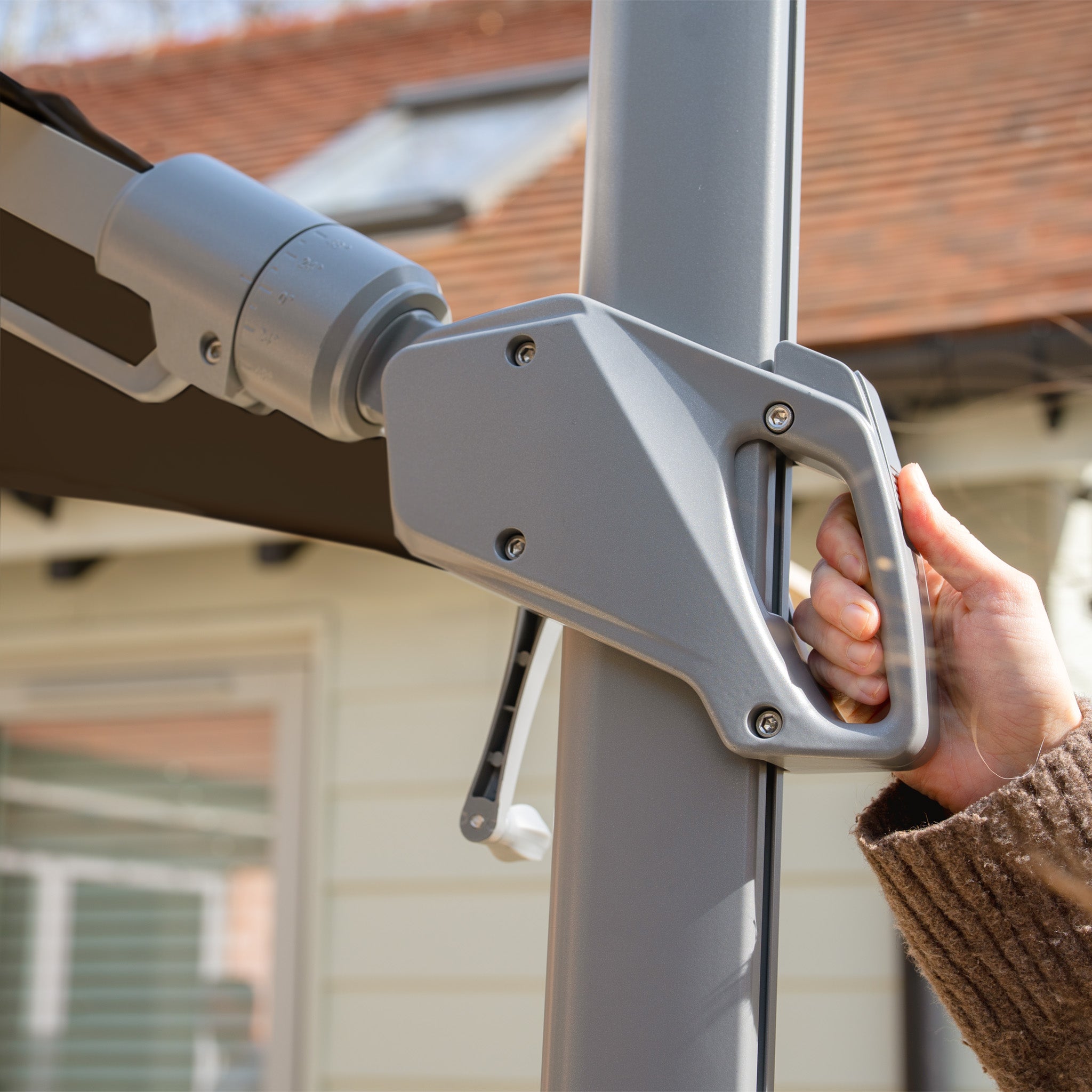 Close-up of someone adjusting the Hera 3m x 2m Rectangular Cantilever Parasol with LED Lighting in Charcoal using its handle mechanism outdoors.