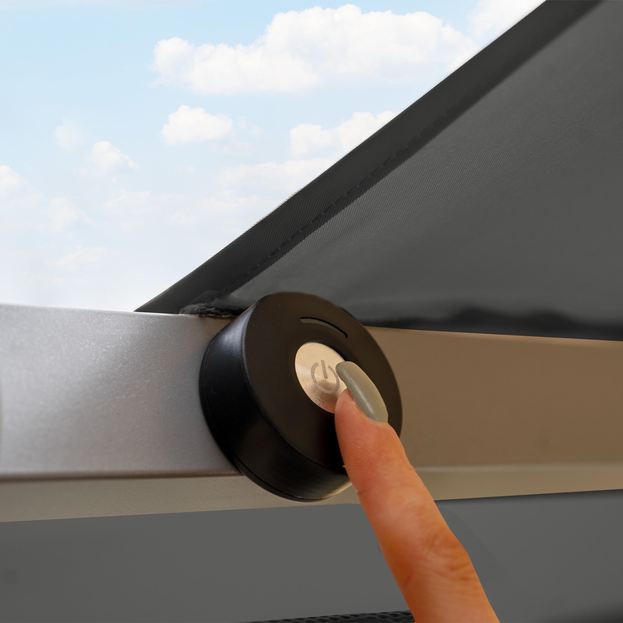 A finger presses the power button on the sleek surface of the Hera 3m Round Cantilever Parasol with LED Lighting in Charcoal, as its understated LED lights glow subtly against a cloudy sky backdrop.