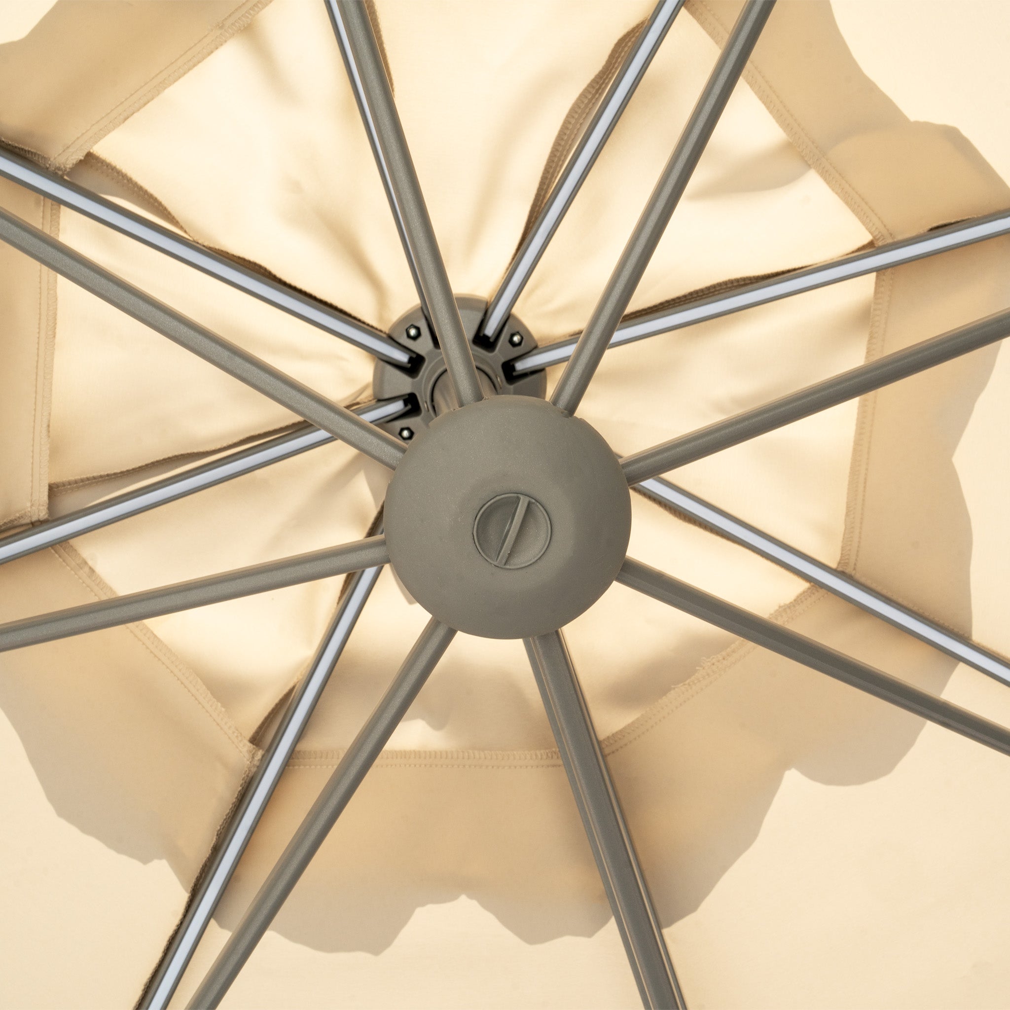 View from beneath a beige Hera 3m Round Cantilever Parasol with LED Lighting, showcasing its symmetrical spokes and central hub. Relax under its elegant UV50+ protective shade.