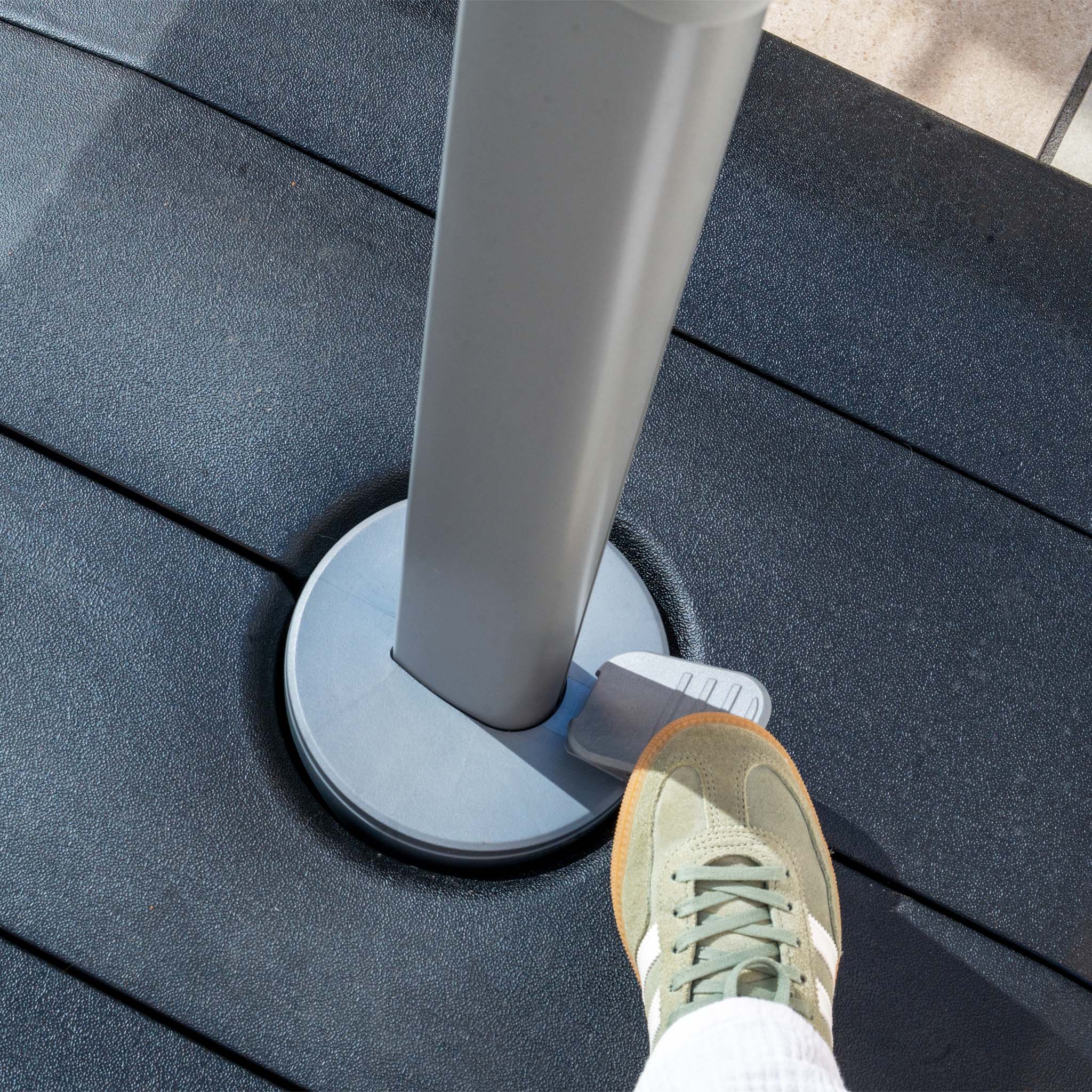 By stepping on the pedal of the Hera 3m Round Cantilever Parasol with LED Lighting in Beige, a person can adjust its metal pole base on a dark surface, ensuring optimal shade with UV50+ fabric protection.