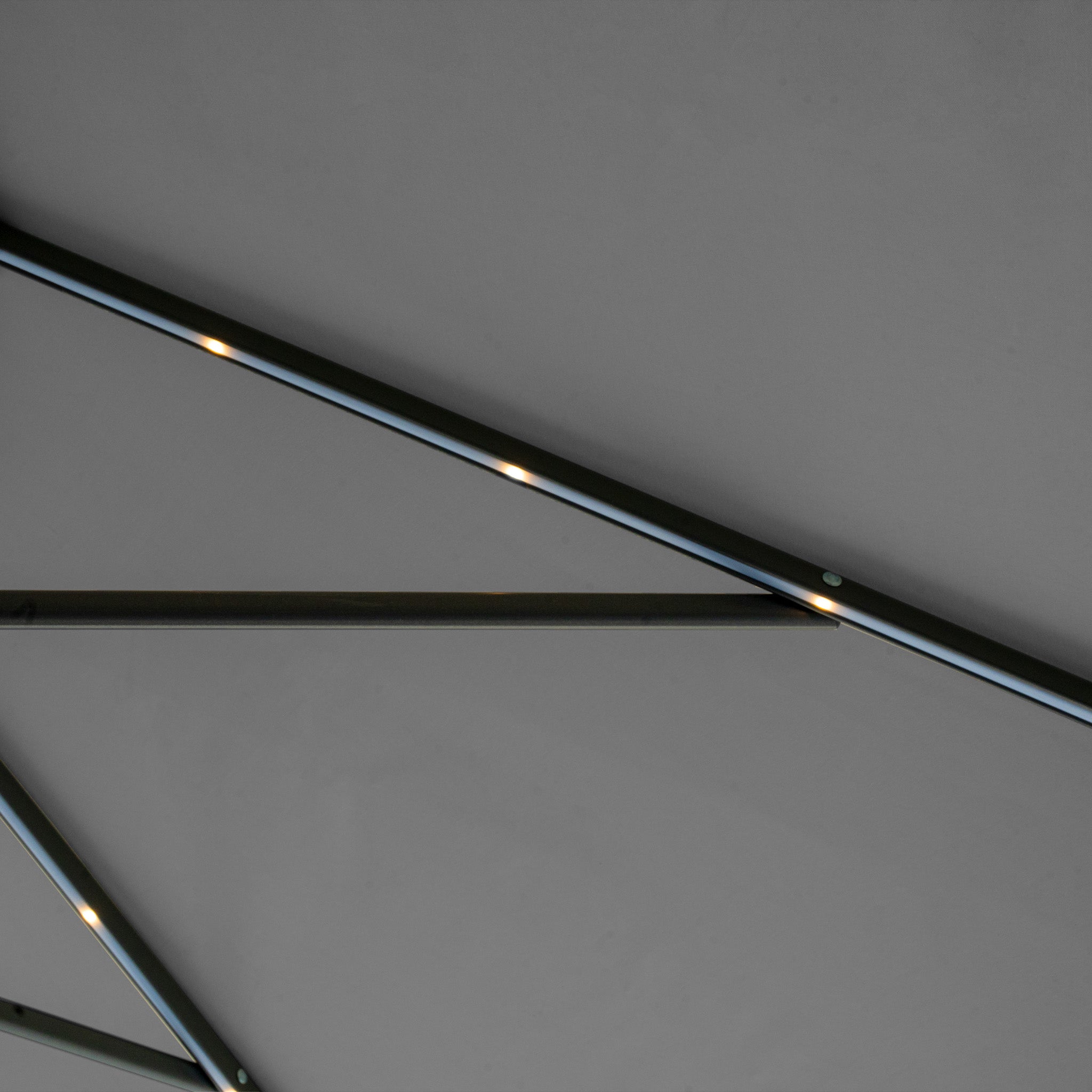 Close-up of the Hera 3m x 2m Rectangular Cantilever Parasol in Charcoal, featuring intersecting beams and LED lights against a gray background.