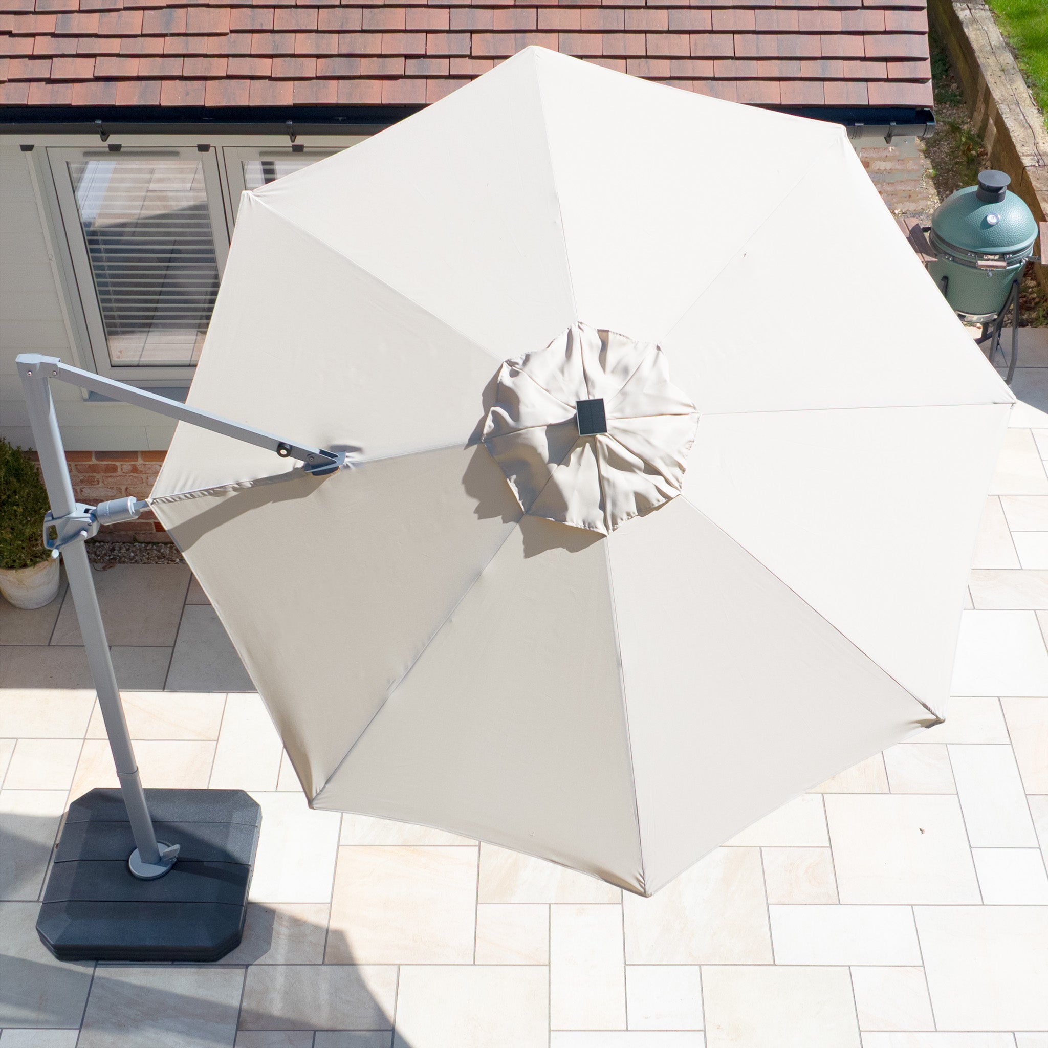 Aerial view of the Hera 3m Round Cantilever Parasol with LED Lighting in Beige, featuring UV50+ fabric, on a tiled patio near a green grill.