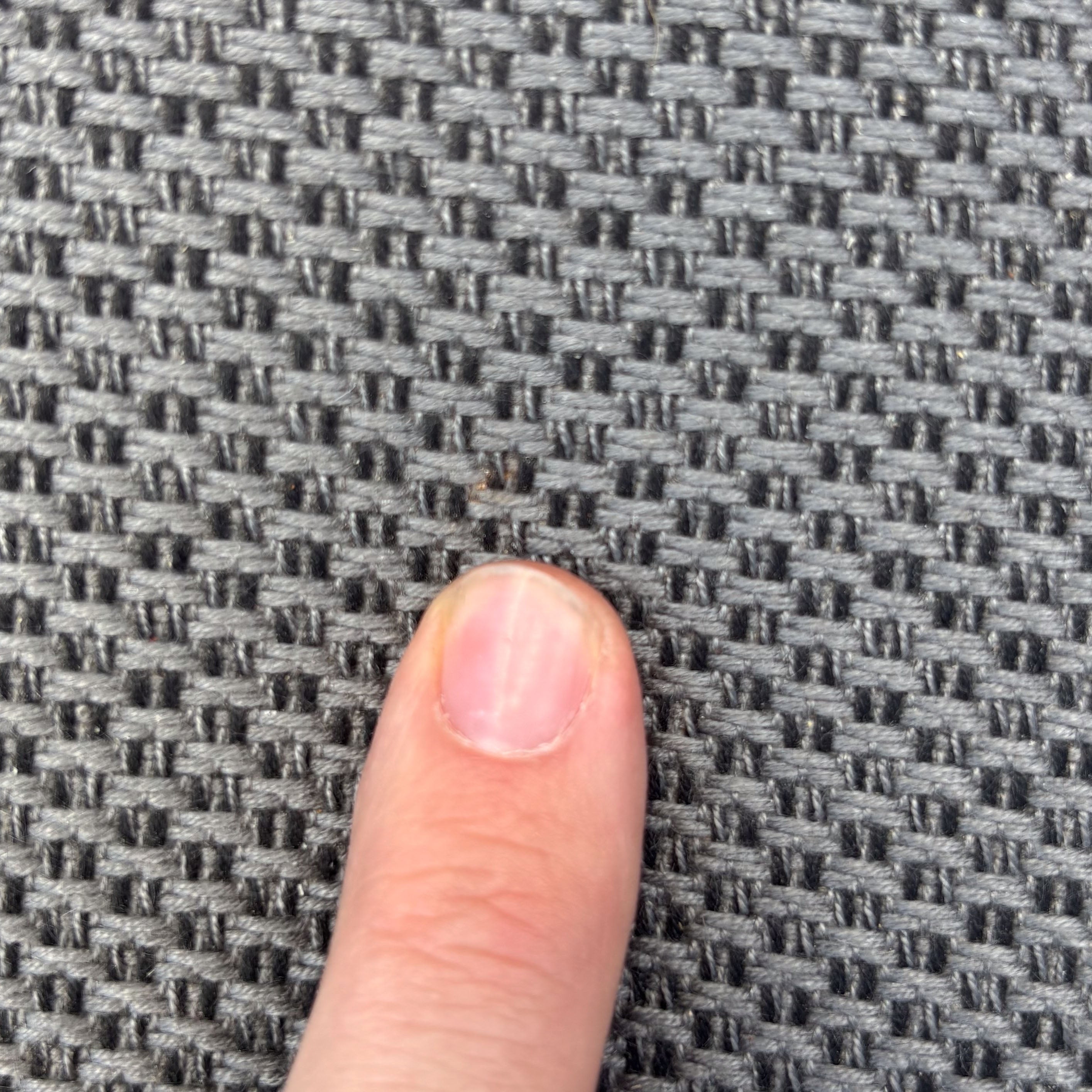 A finger points at a small brown bug on the grey Luna Outdoor Fabric Bar Stool (Ex Display), highlighting its textured surface.
