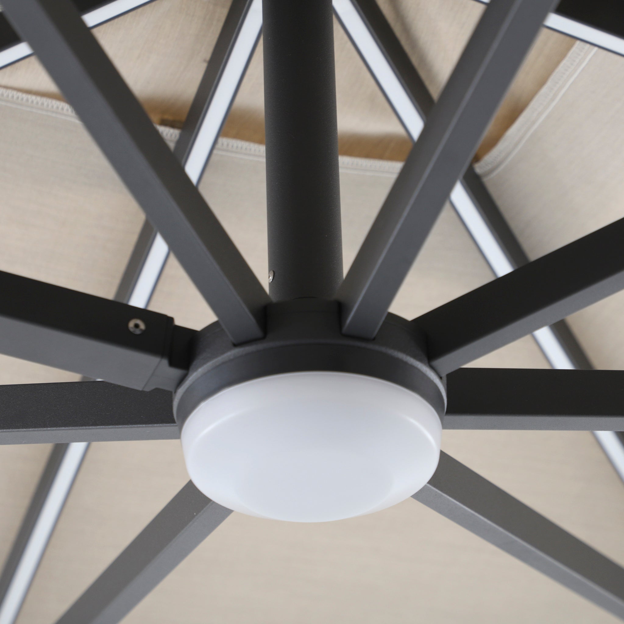 Close-up of the hub and spokes of the Volos 3m x 4m Aluminium Cantilever Parasol with LED lighting and 120kg granite base in Wheat, showing the round LED light fixture attached underneath.