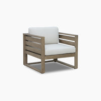 The Andora Armchair in Weathered Brown and Linen features weather-resistant eucalyptus wood, light beige cushions, slatted sides, and a boxy design—ideal for stylish outdoor seating.