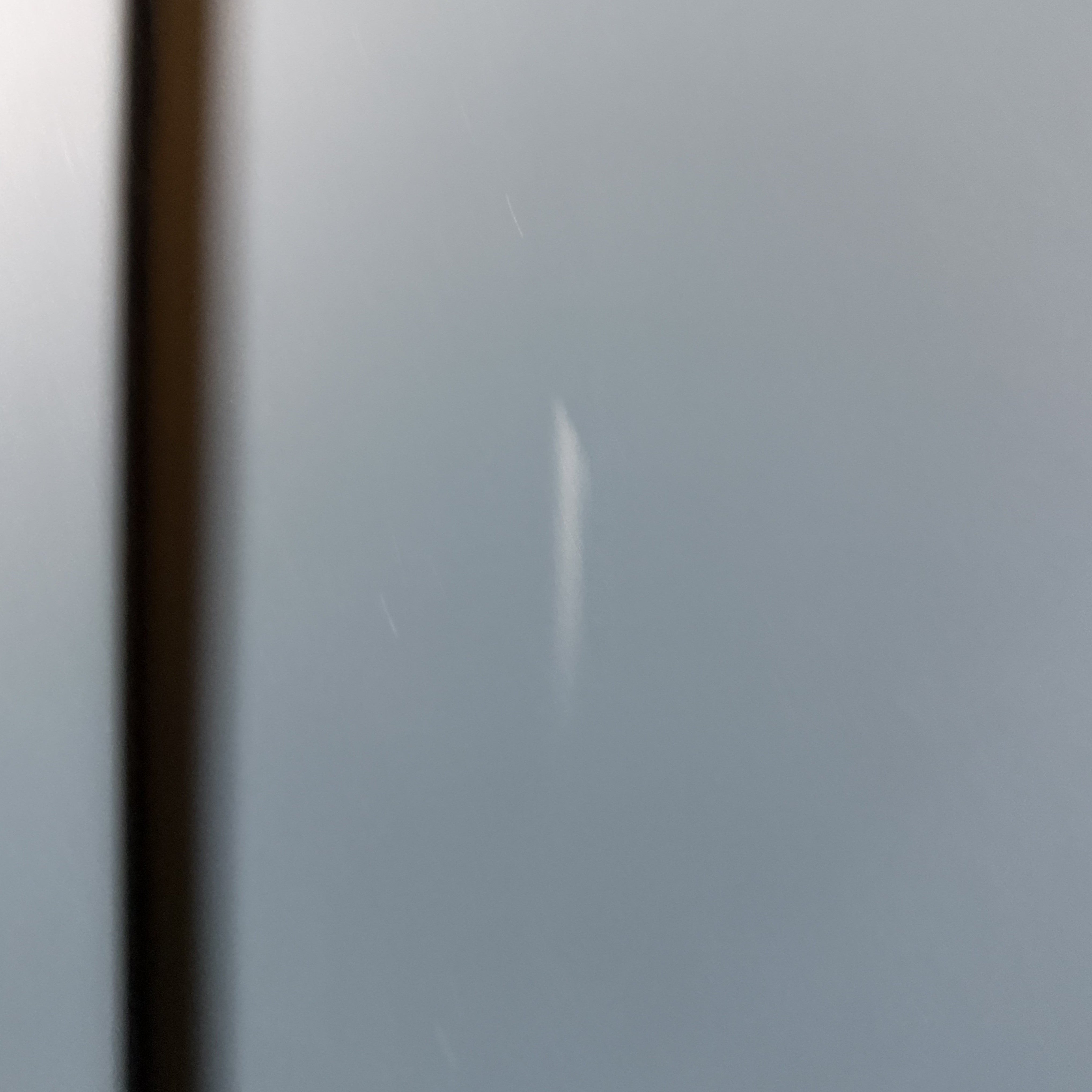 Blurry image of a light gray surface with a vertical scratch and a black edge on the left, possibly part of a Burford Triple Larder Unit in Navy Blue (Ex Display).