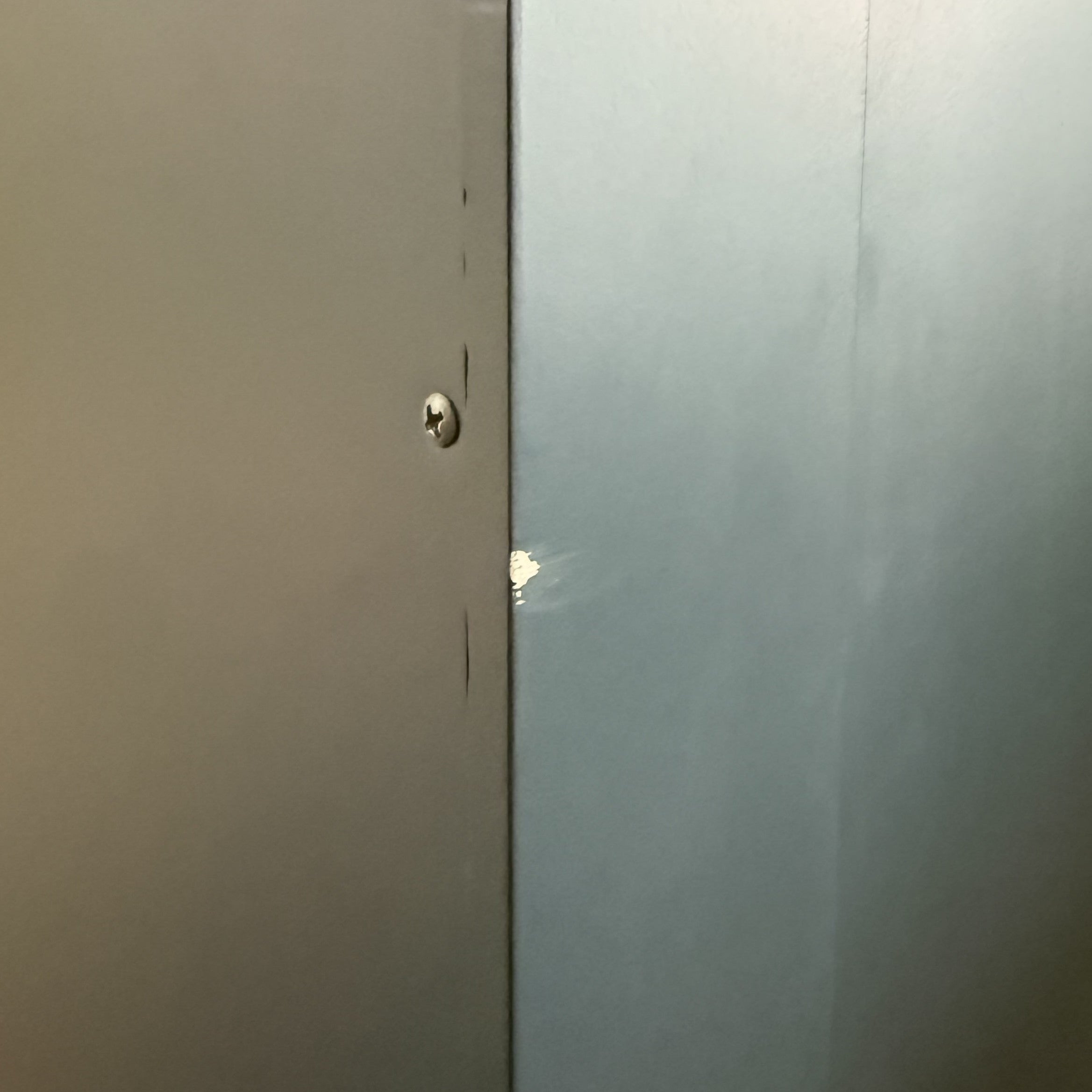 A gray metal door is beside the Burford Triple Larder Unit in Navy Blue (Ex Display), with a small chipped paint spot on the wall near the edge.