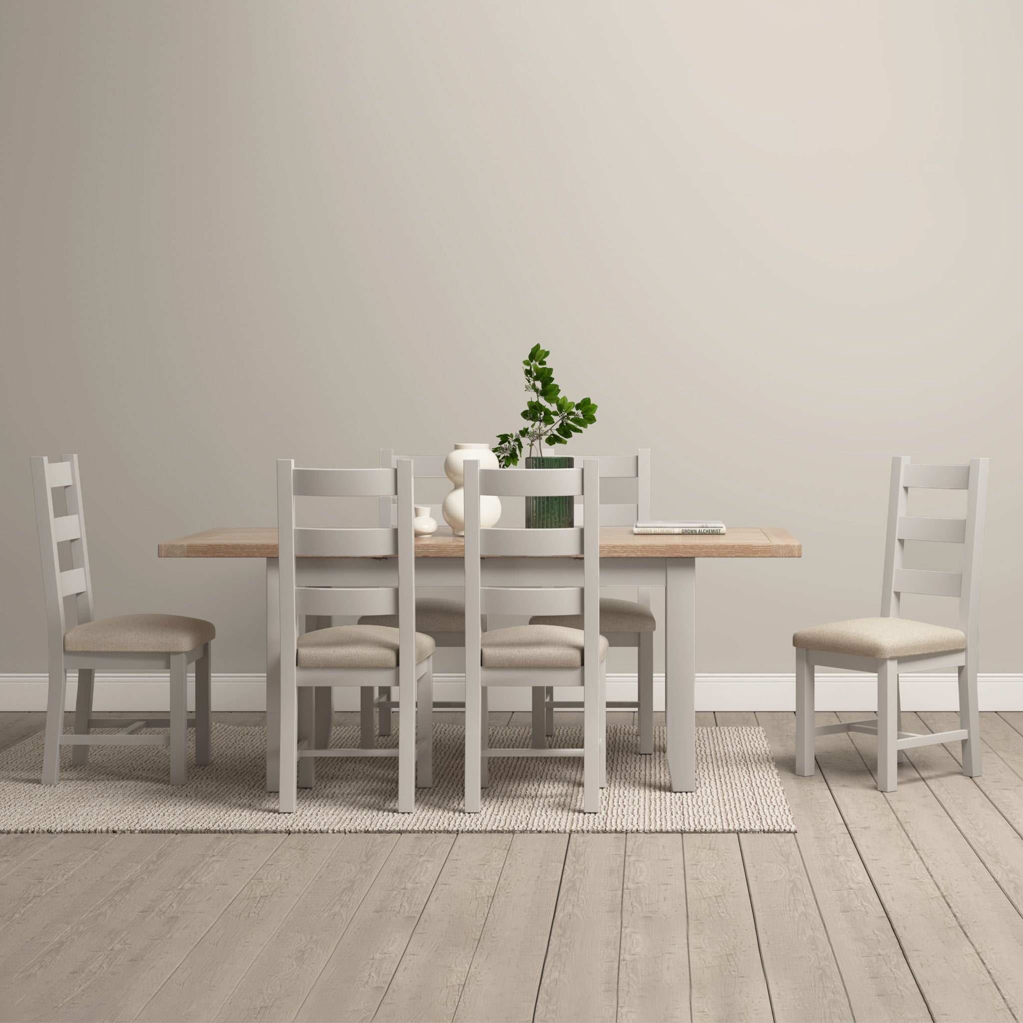 A minimalist dining room showcases the Burford 6 Seat Extending Dining Set in Pebble Grey, with six chairs and a small plant centerpiece on a textured rug, exuding contemporary elegance.