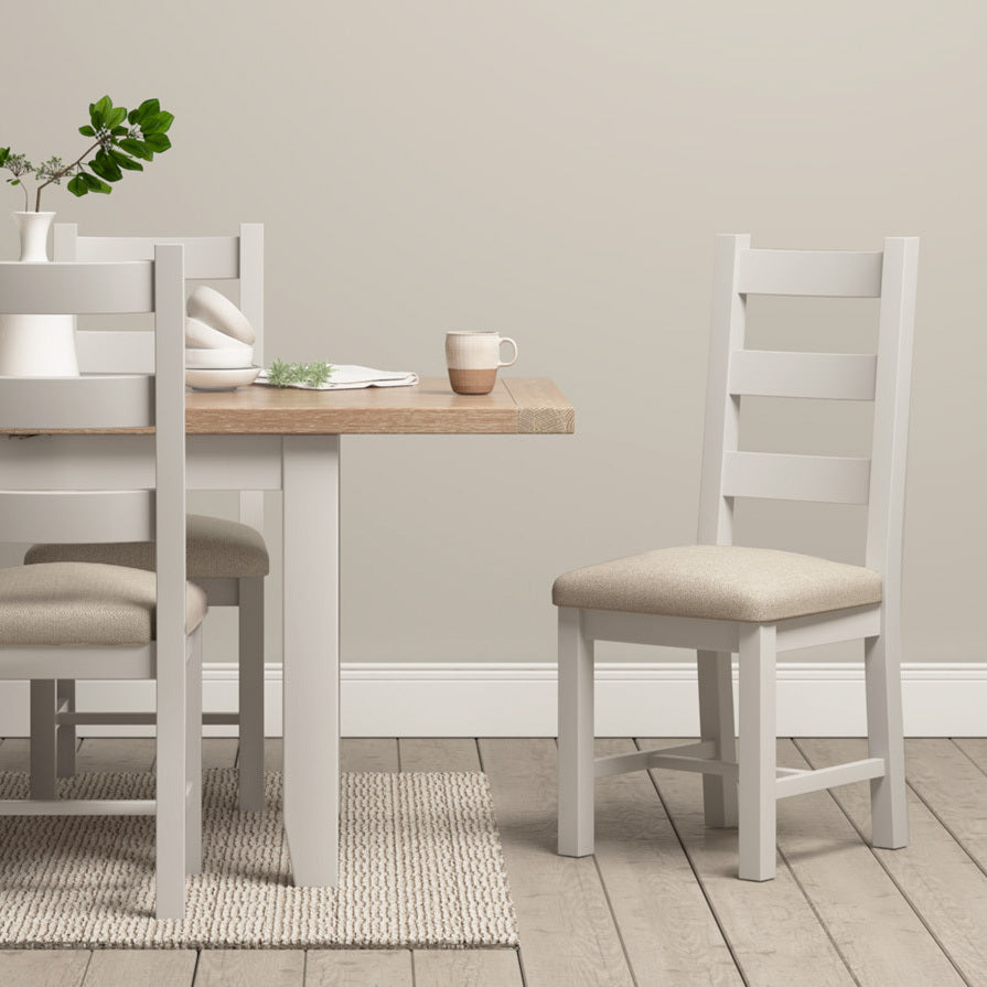 Minimalist dining area with a Burford 6 Seat Extending Dining Set in Pebble Grey, white chairs, a small plant, and a mug on a beige rug adding subtle elegance.