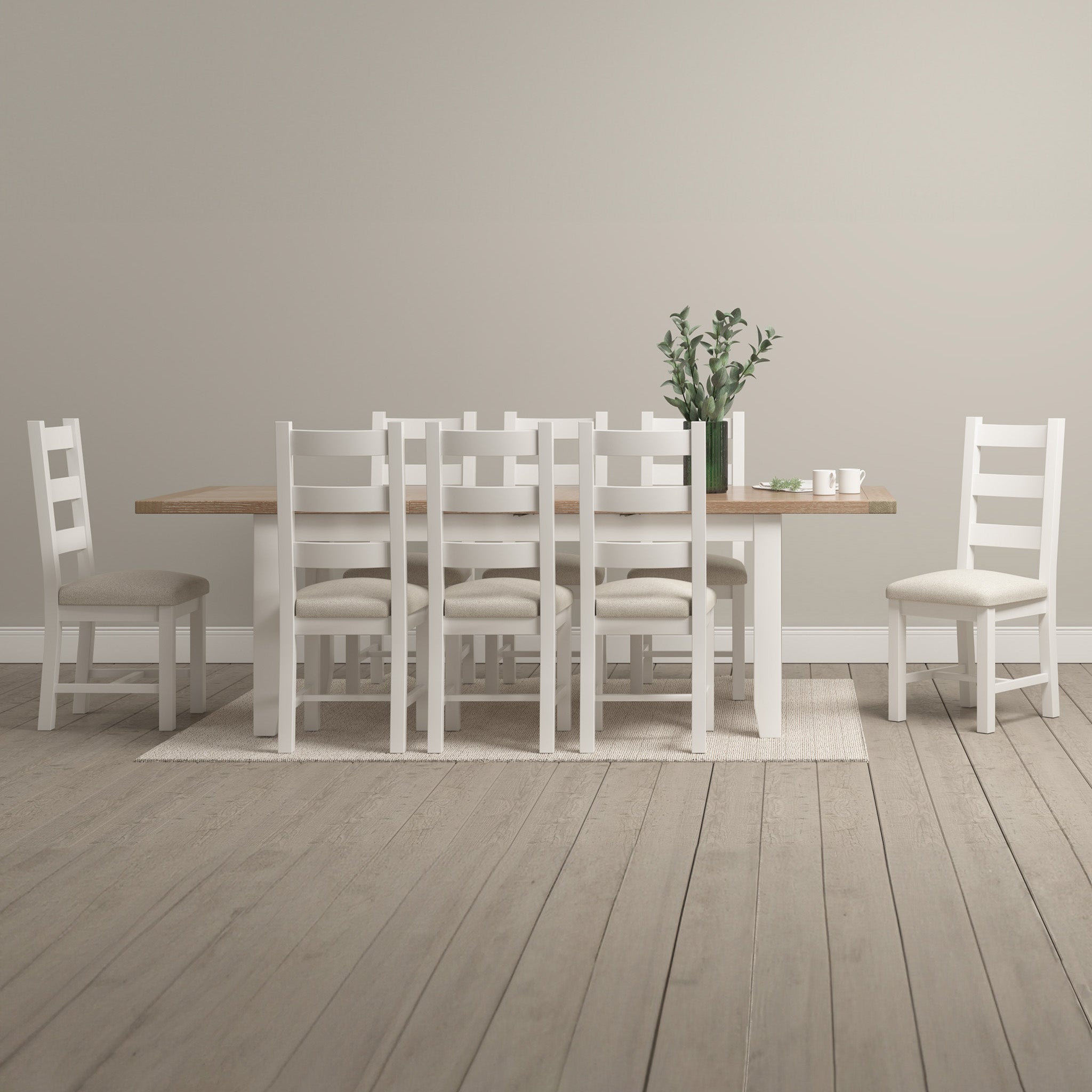 The Burford 8 Seat Extending Dining Set in Warm White includes a spacious table with eight chairs, styled with green leaves and cups on a light rug in a minimalist room.