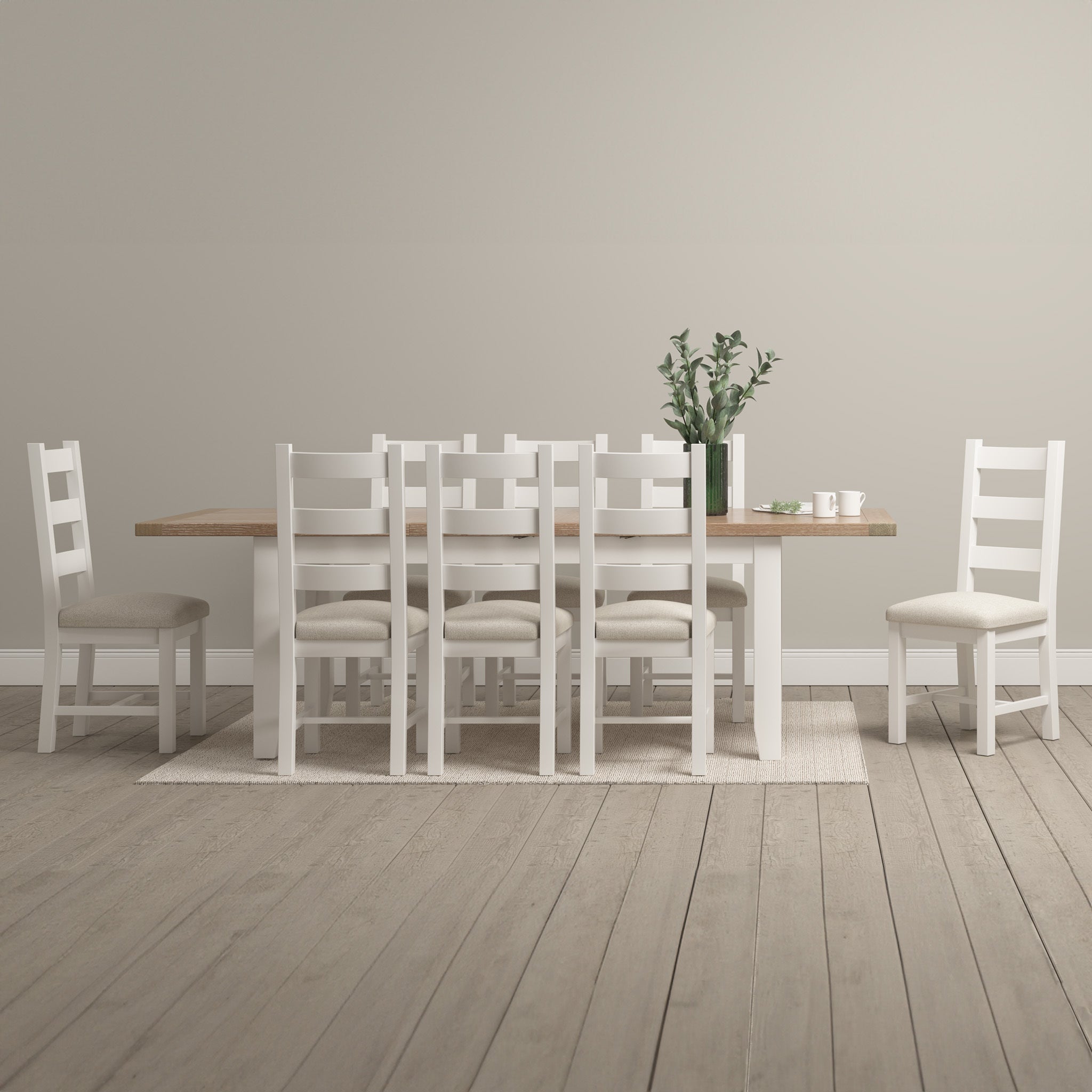 A dining room with a warm white Burford 8 Seat Extending Dining Set, cushioned chairs, a vase of greenery as the centerpiece, and cups with saucers on a light rug.