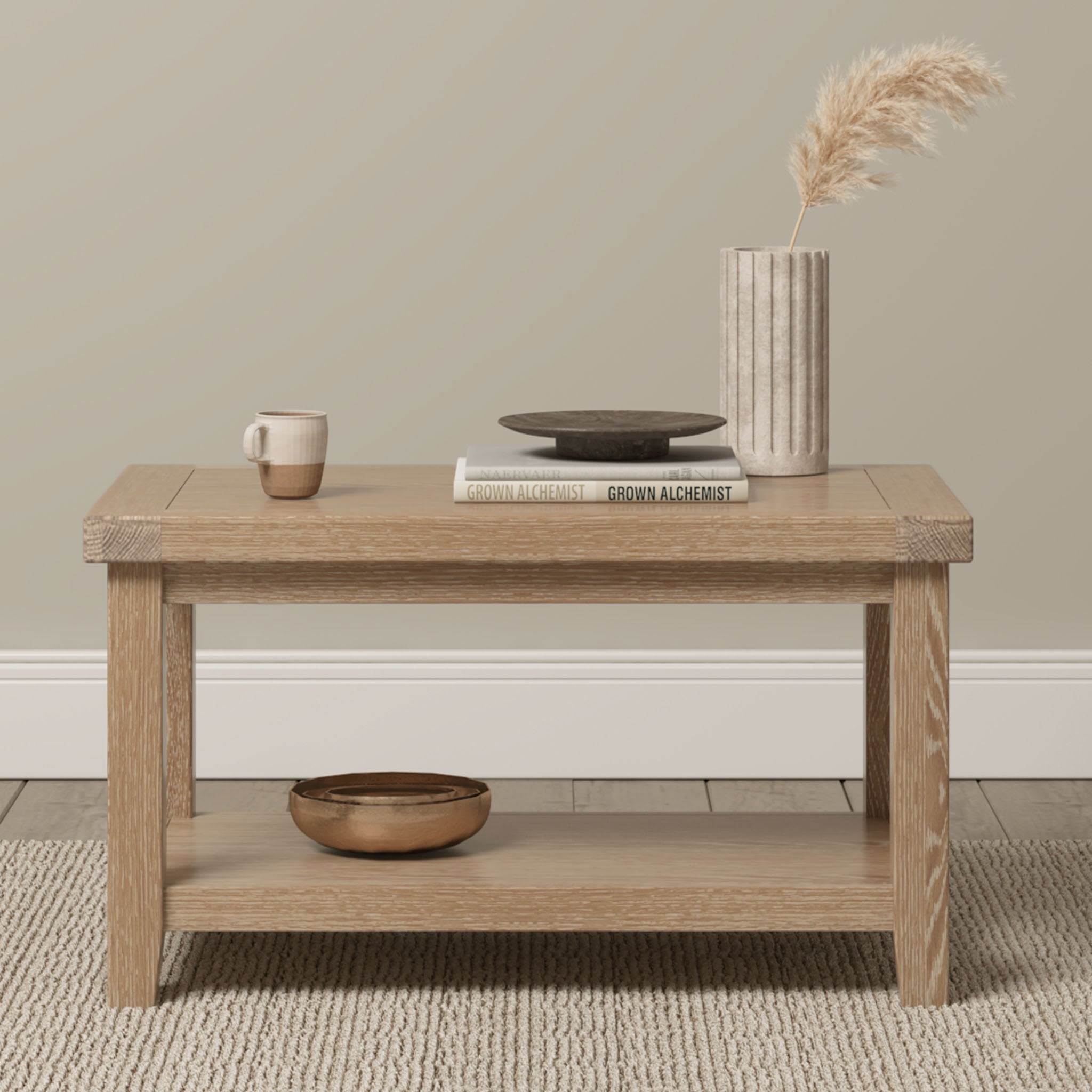 Burford Large Coffee Table with Shelf in Natural Oak shown styled with a cup, books, plate, vase with pampas grass, and a bowl on the lower shelf.