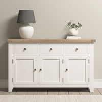 Burford Large 3 Door 3 Drawers Sideboard in Warm White with an oak top, styled with a gray lamp and a vase with greenery.