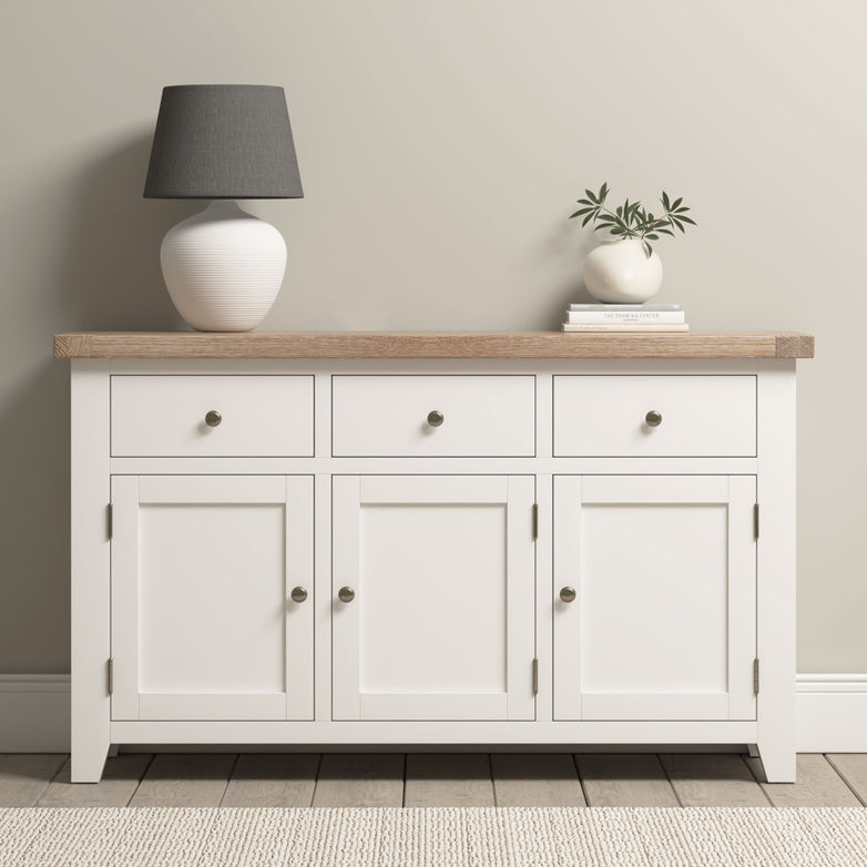 Burford Large 3 Door 3 Drawers Sideboard in Warm White with an oak top, styled with a gray lamp and a vase with greenery.