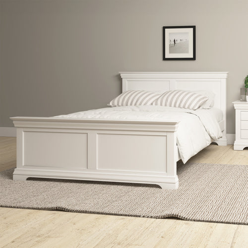 A warm white painted double bed with a rug underneath it