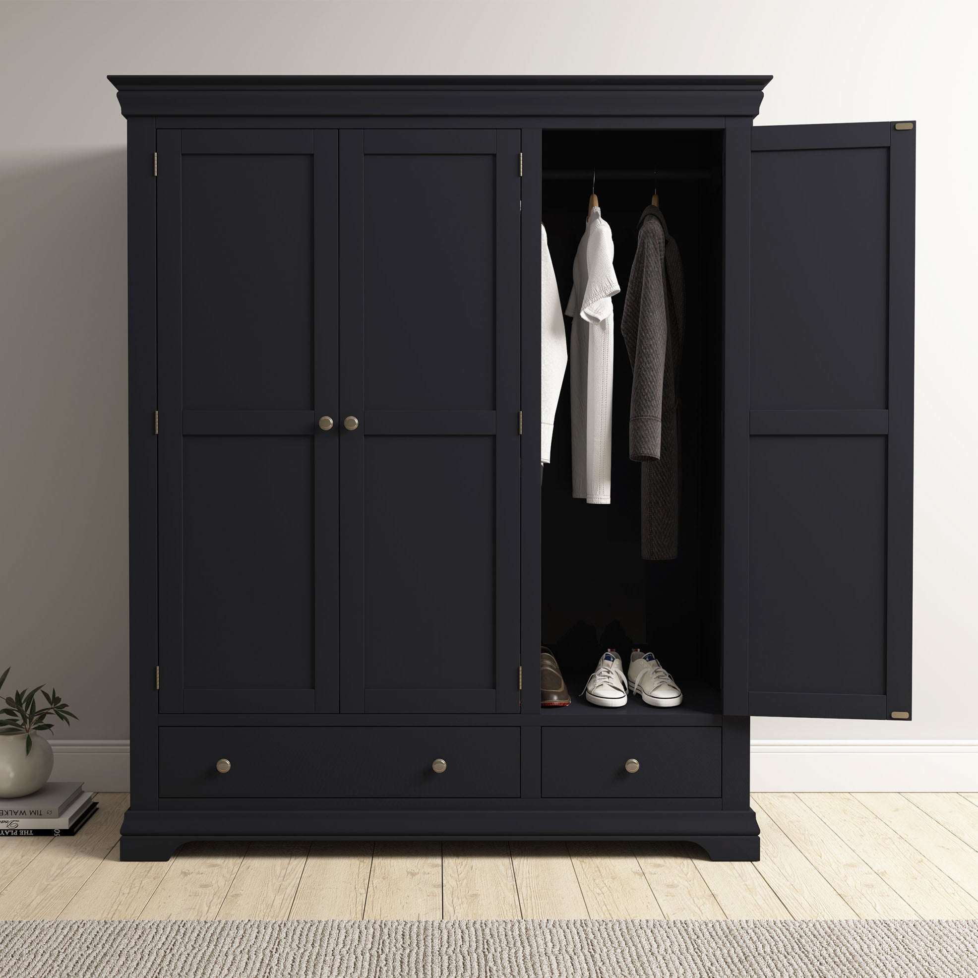 The Chalbury Triple Wardrobe in Dusky Black features open doors revealing hanging clothes and shoes, ideal for adding a modern touch to any wooden-floored bedroom.