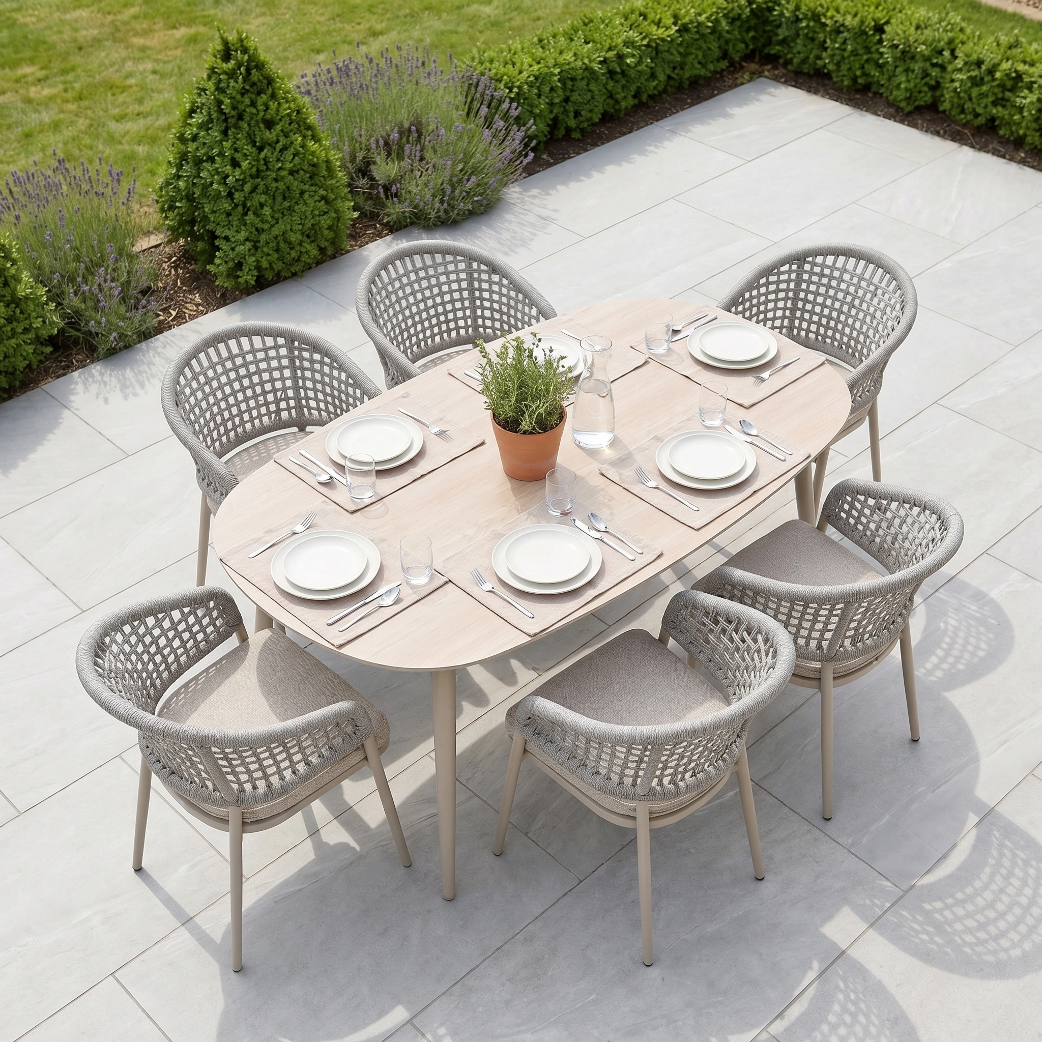 The Kalama 6 Seat Oval Rope Dining Set in Oatmeal features neutral chairs, white dishes, and a potted plant centerpiece—an inviting ensemble that brings style and comfort to your patio dining.