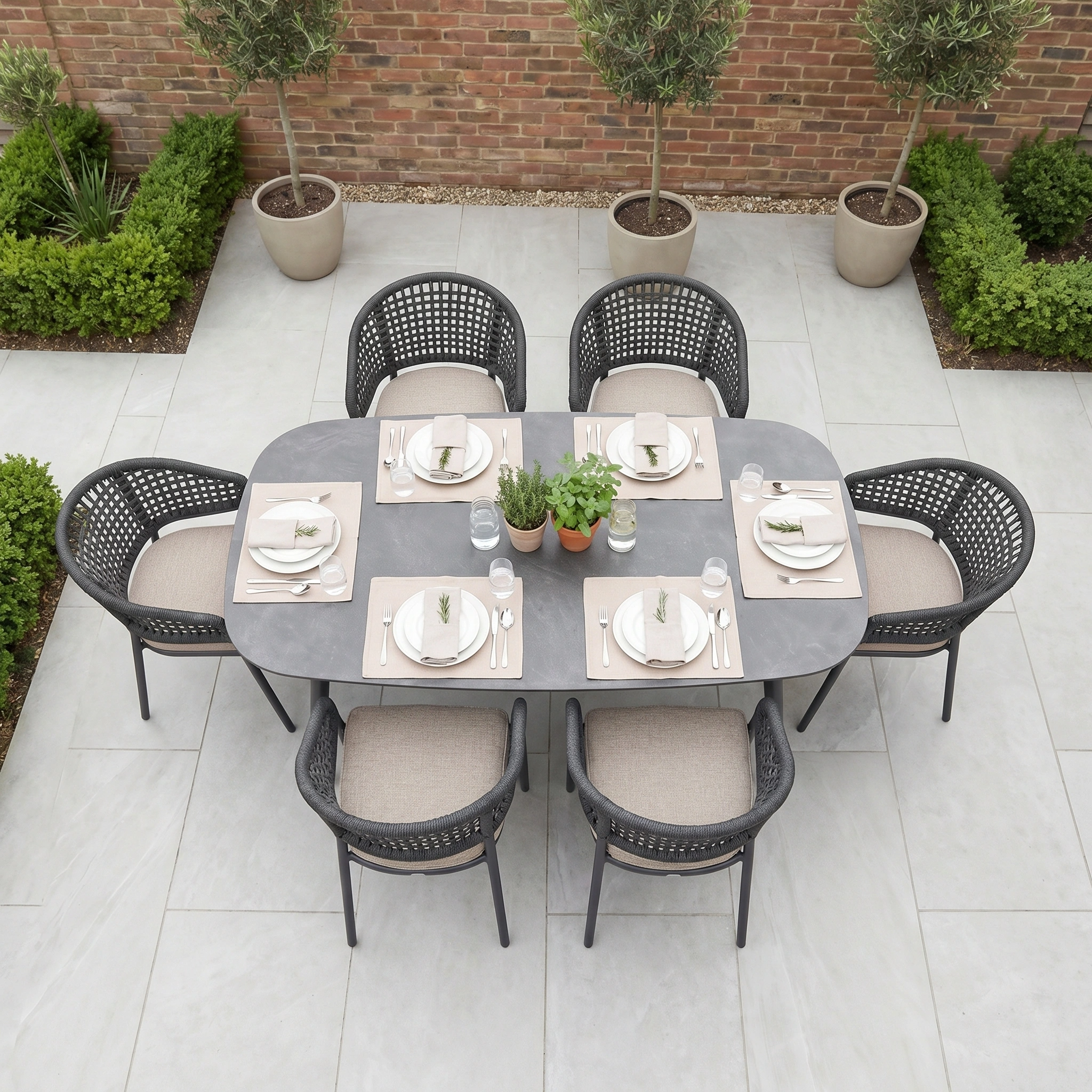 The Kalama 6 Seat Oval Rope Dining Set in Truffle, styled with plants, neutral dishes, and woven chairs, creates a stylish dining space on your patio—perfect garden furniture for outdoor gatherings.