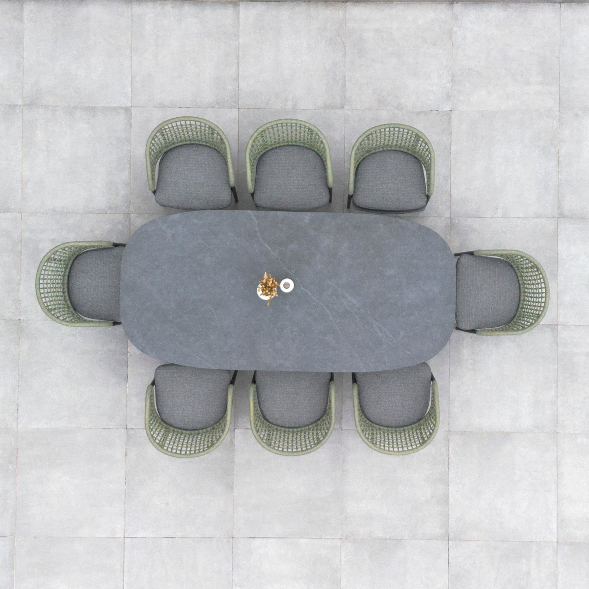 A top view reveals an oval table with a stylish centerpiece, surrounded by seven woven chairs on a tiled floor. Crafted with weather-proof aluminum, this intricate setup evokes the elegance of the Kalama 8 Seat Rope Oval Dining Set with Ceramic Table in Olive Green.