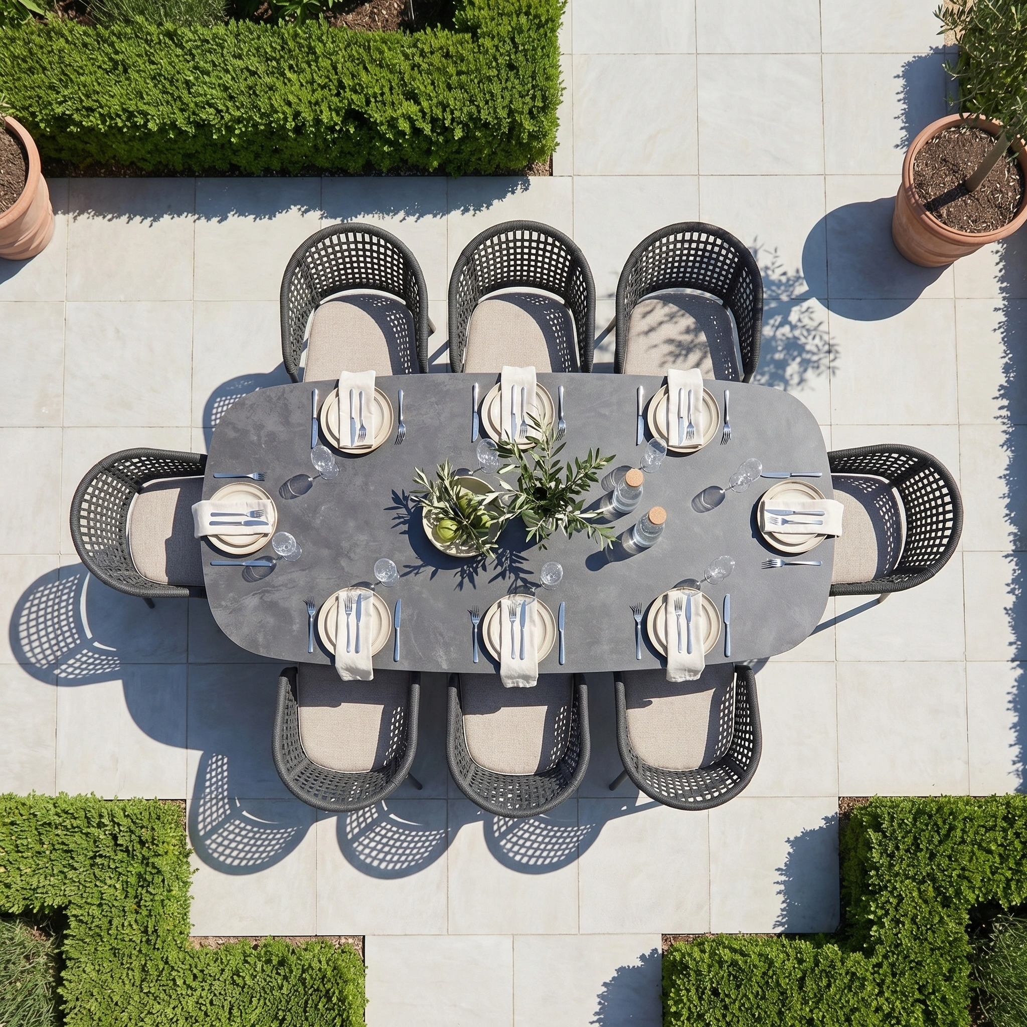 A top-down view of the Kalama 8 Seat Oval Rope Dining Set in Truffle highlights a modern outdoor dining set for eight, surrounded by greenery and potted plants—an ideal example of stylish garden furniture.