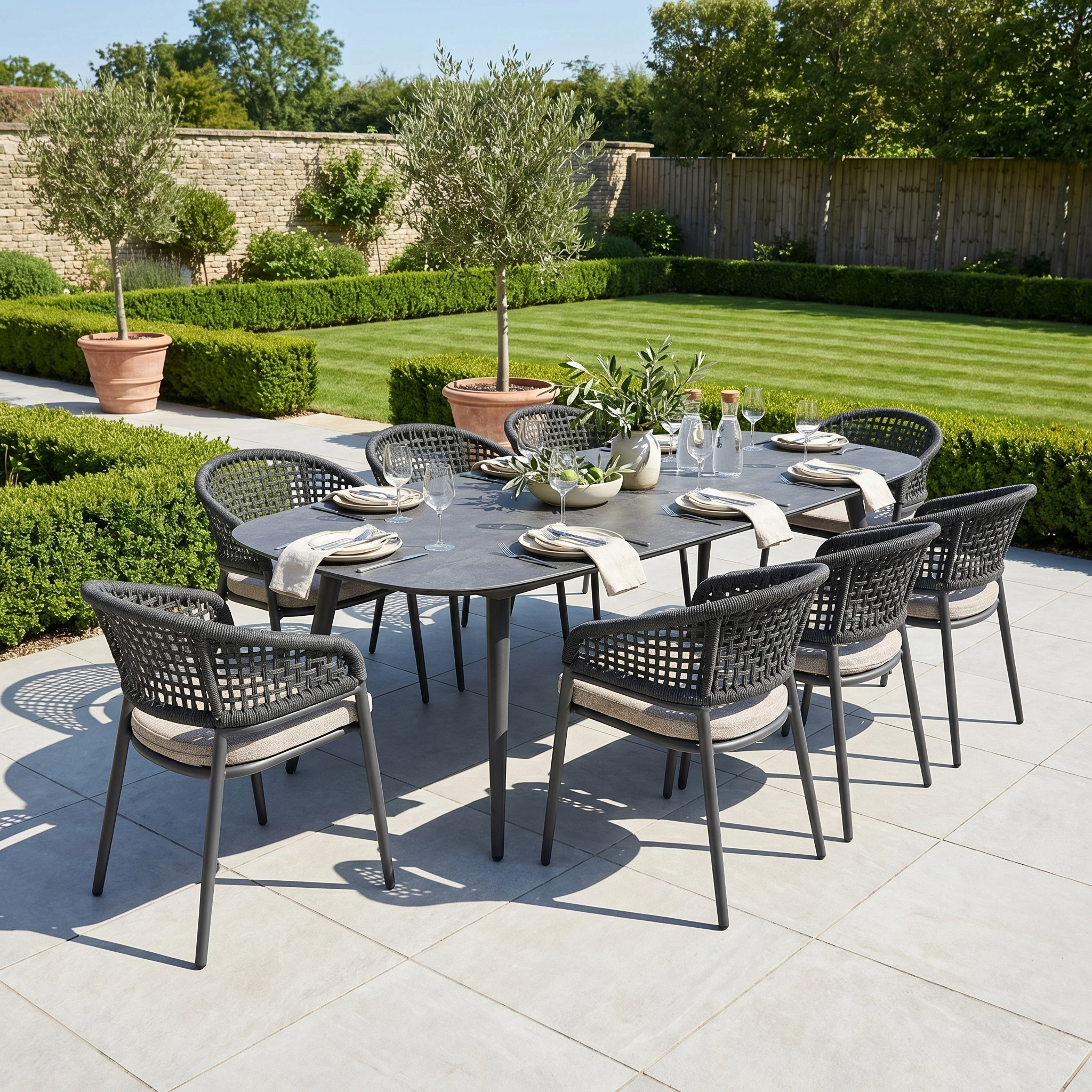 A modern outdoor dining set, the Kalama 8 Seat Oval Rope Dining Set in Truffle features stylish aluminium and rope furniture, perfect for patios framed by greenery and manicured hedges.