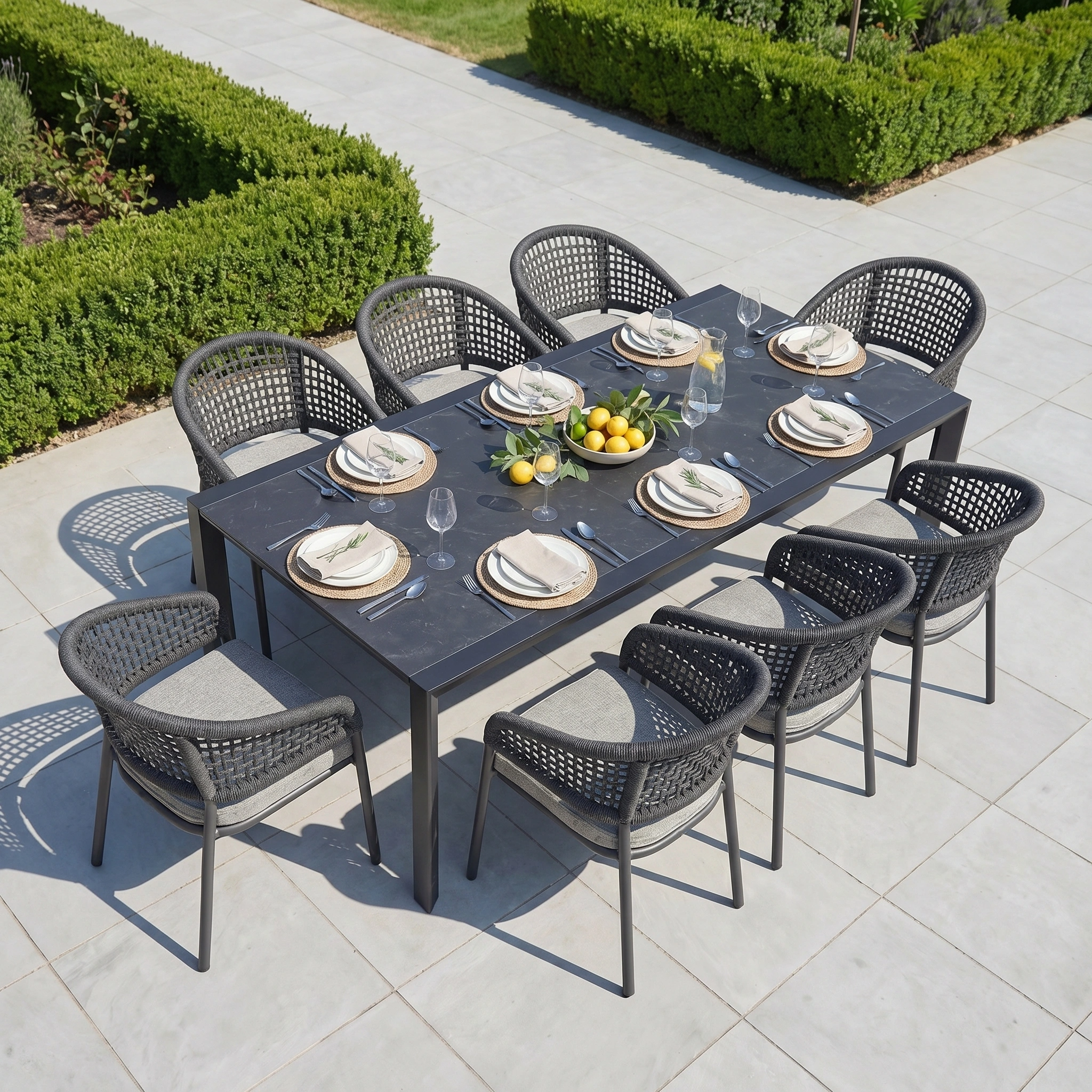 The Kalama 8 Seat Extending Dining Set with Ceramic Table in Truffle features durable aluminium construction, perfect for stylish outdoor gatherings with plates, glasses, and lemons on the patio surrounded by wicker chairs.