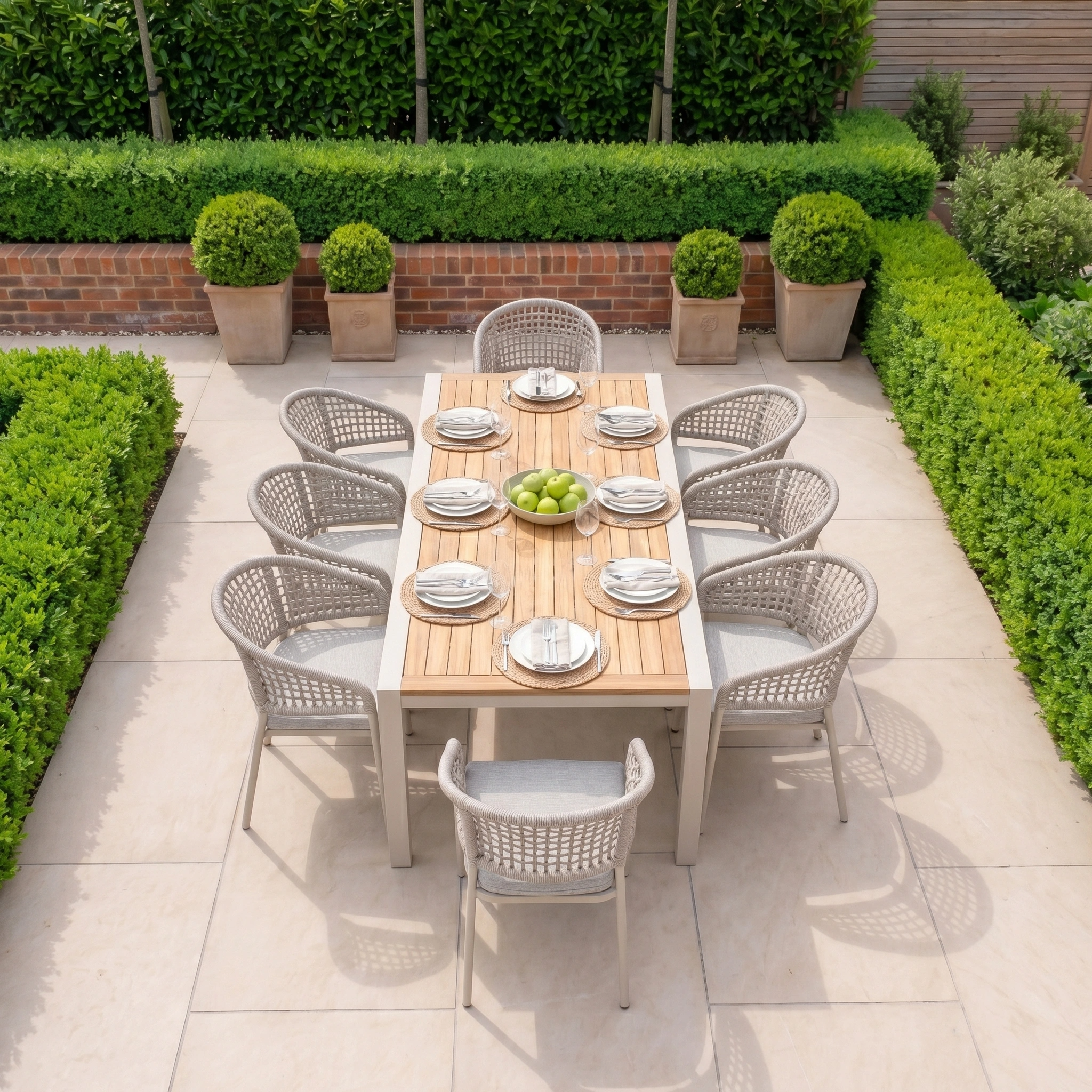 The Kalama 8 Seat Extending Dining Set with Teak Table in Oatmeal is set on a stylish tiled patio, surrounded by lush greenery and potted plants for an inviting outdoor dining experience.