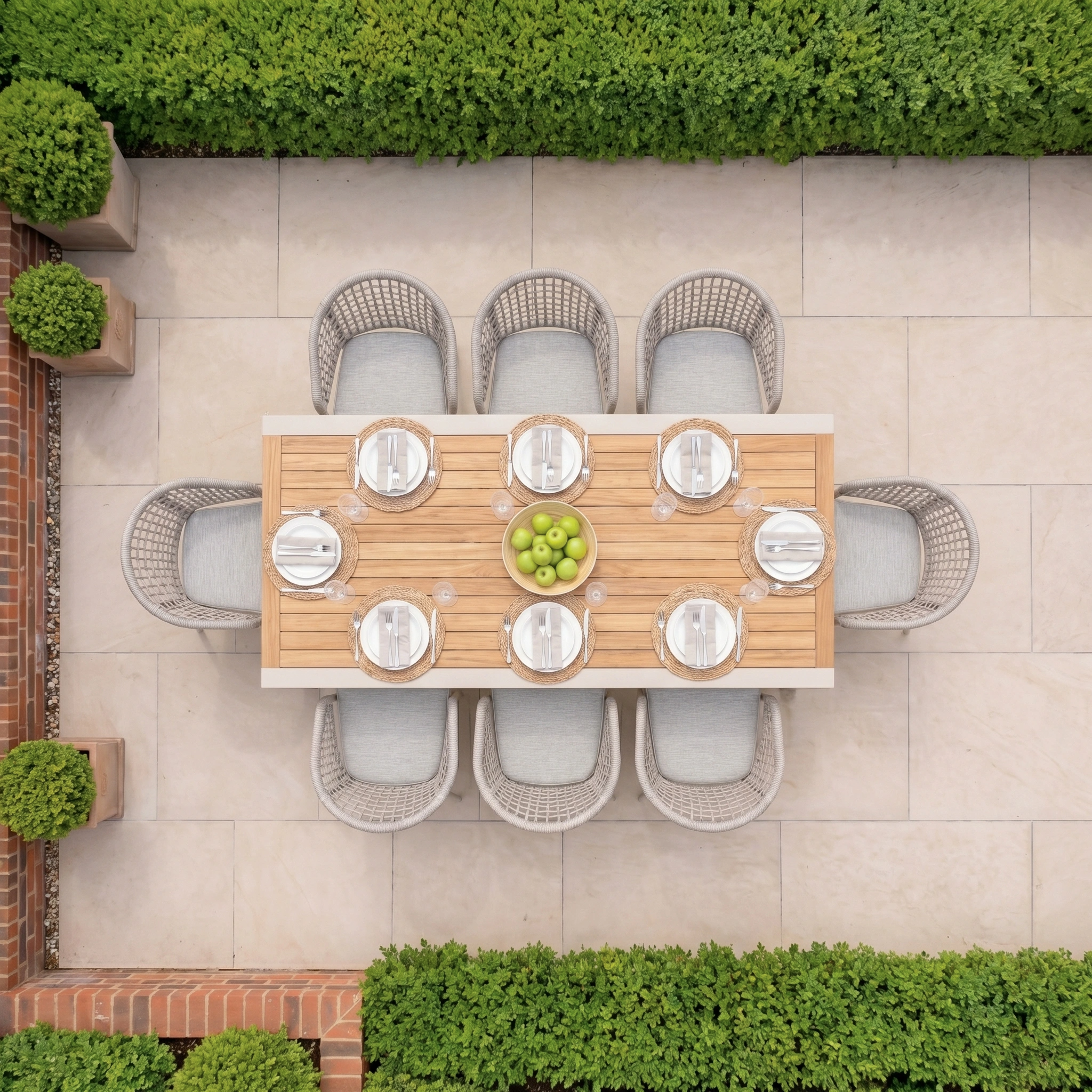 Top view of a patio featuring the Kalama 8 Seat Extending Dining Set with Teak Table in Oatmeal, surrounded by green hedges and potted plants.