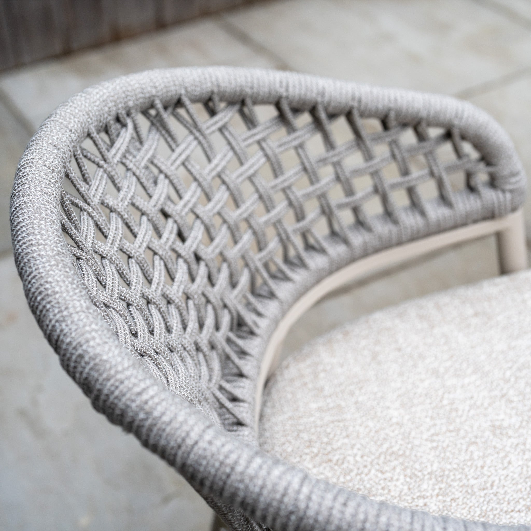 Close-up of a chair from the Kalama 4 Seat Round Rope Dining Set with Albatross Table in Oatmeal, showing its woven textured backrest and cushioned neutral seat.