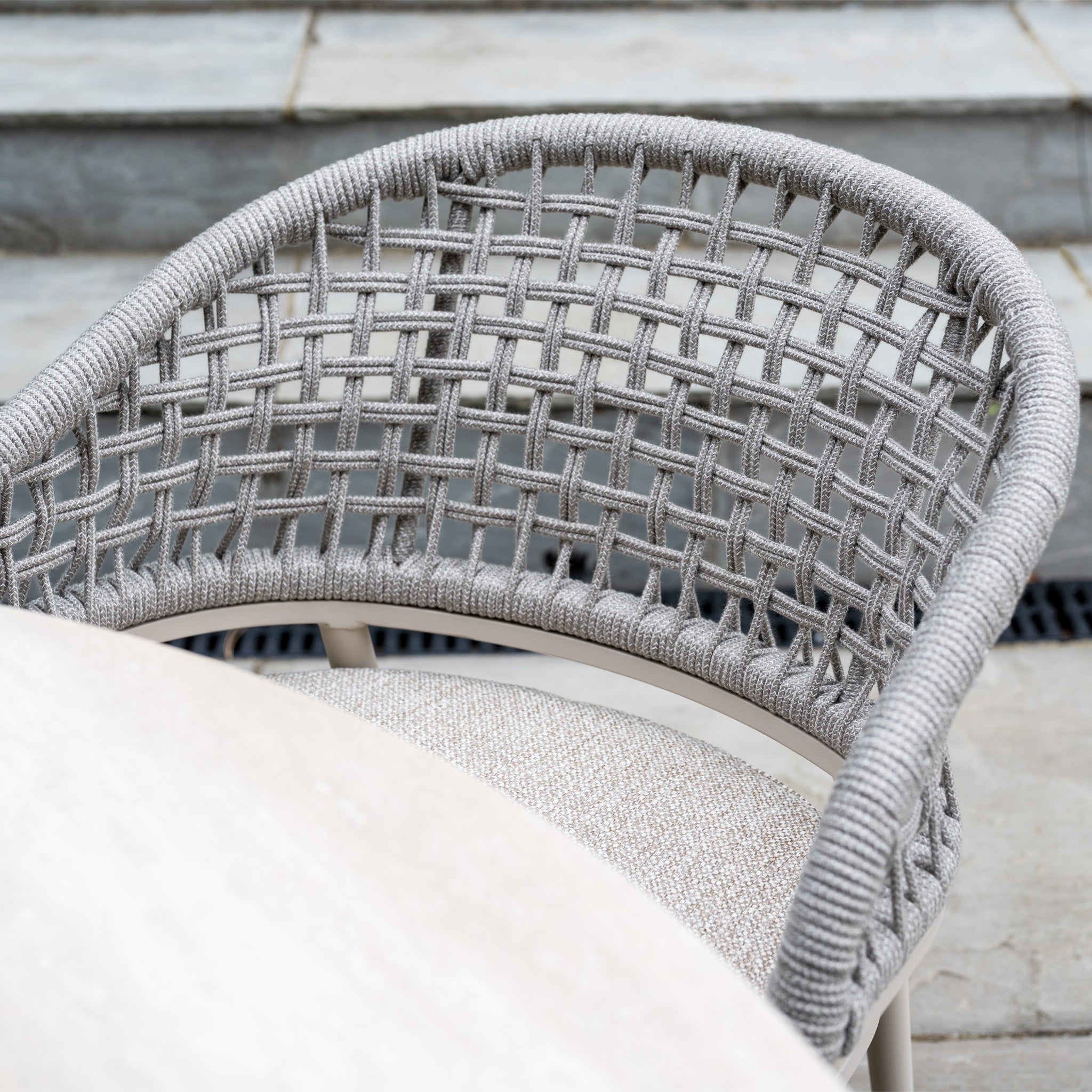 The Kalama 4 Seat Round Rope Dining Set with Albatross Table in Oatmeal creates a stylish garden dining area, featuring elegant chairs and a round table on a stone patio.