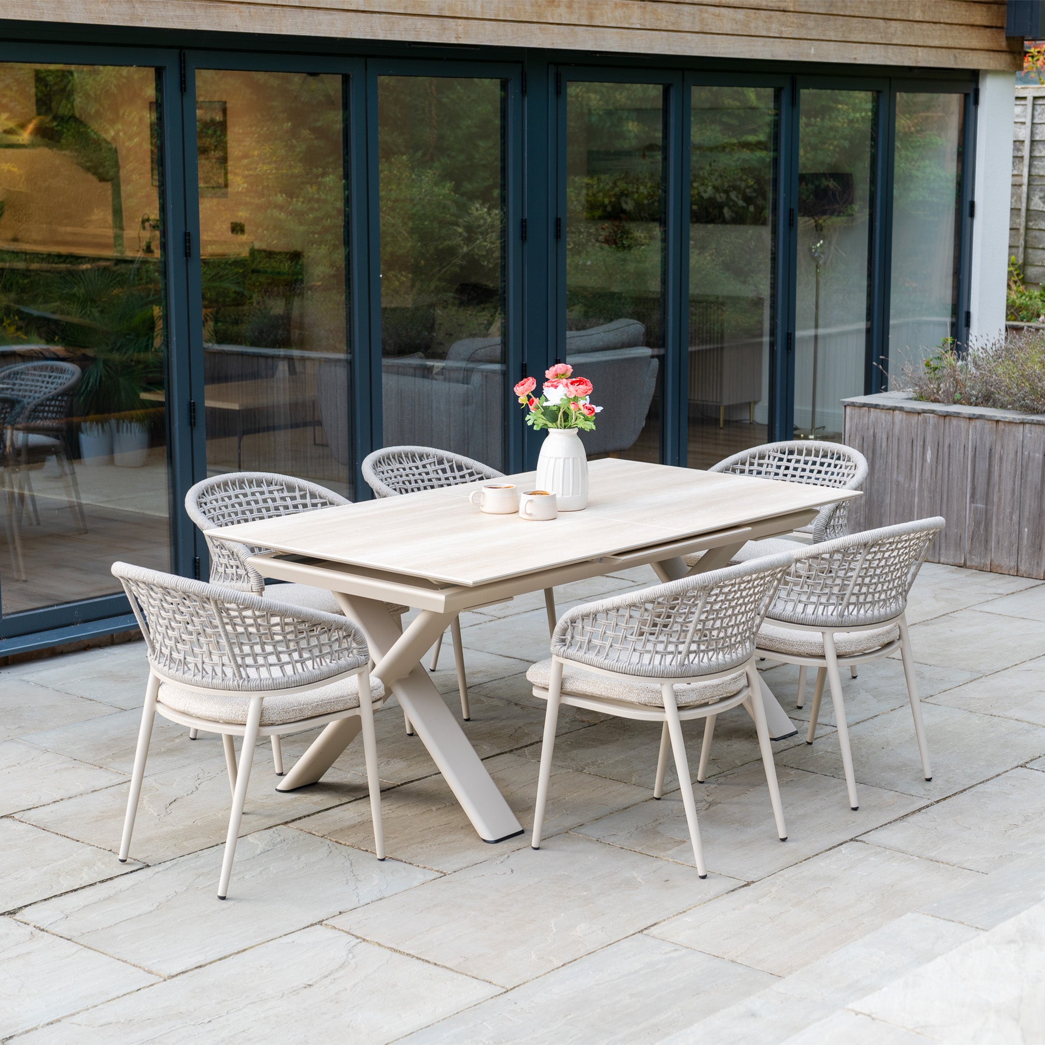 Modern outdoor dining set featuring the Kalama 6 Seat Rope Dining Set with Albatross Extending Table in Oatmeal, shown on a patio with chairs and a white vase of flowers.