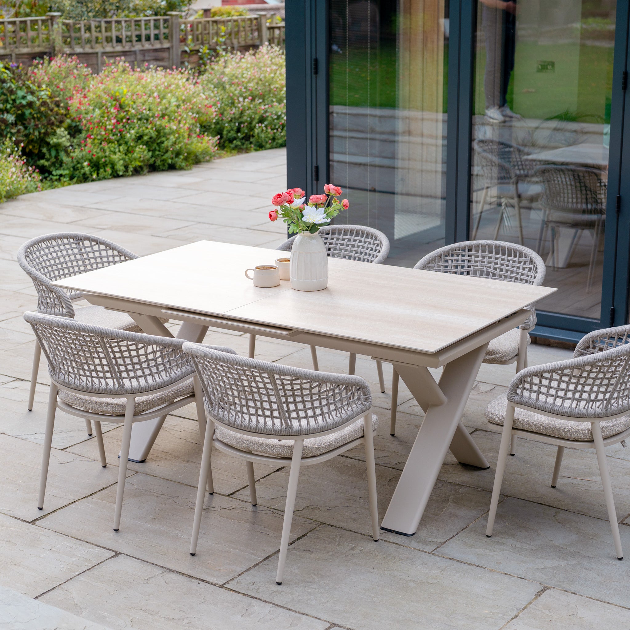 Modern outdoor dining set with six chairs in boucle fabric, vases, and mugs on a stone patio—ideal for gatherings around the Kalama 6 Seat Rope Dining Set with Albatross Extending Table in Oatmeal.