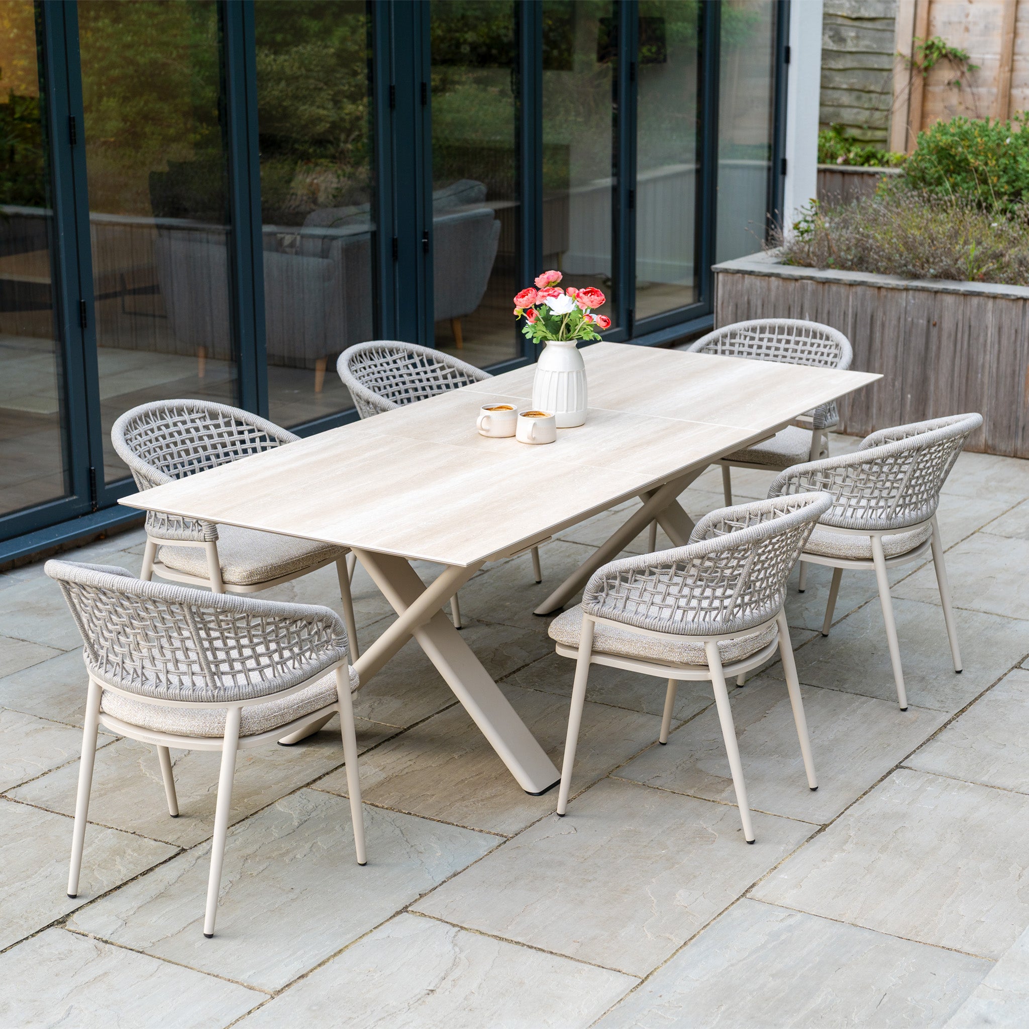The Kalama 6 Seat Rope Dining Set with Albatross Extending Table in Oatmeal features six woven chairs and a sleek extending table, perfect for outdoor meals on the patio.