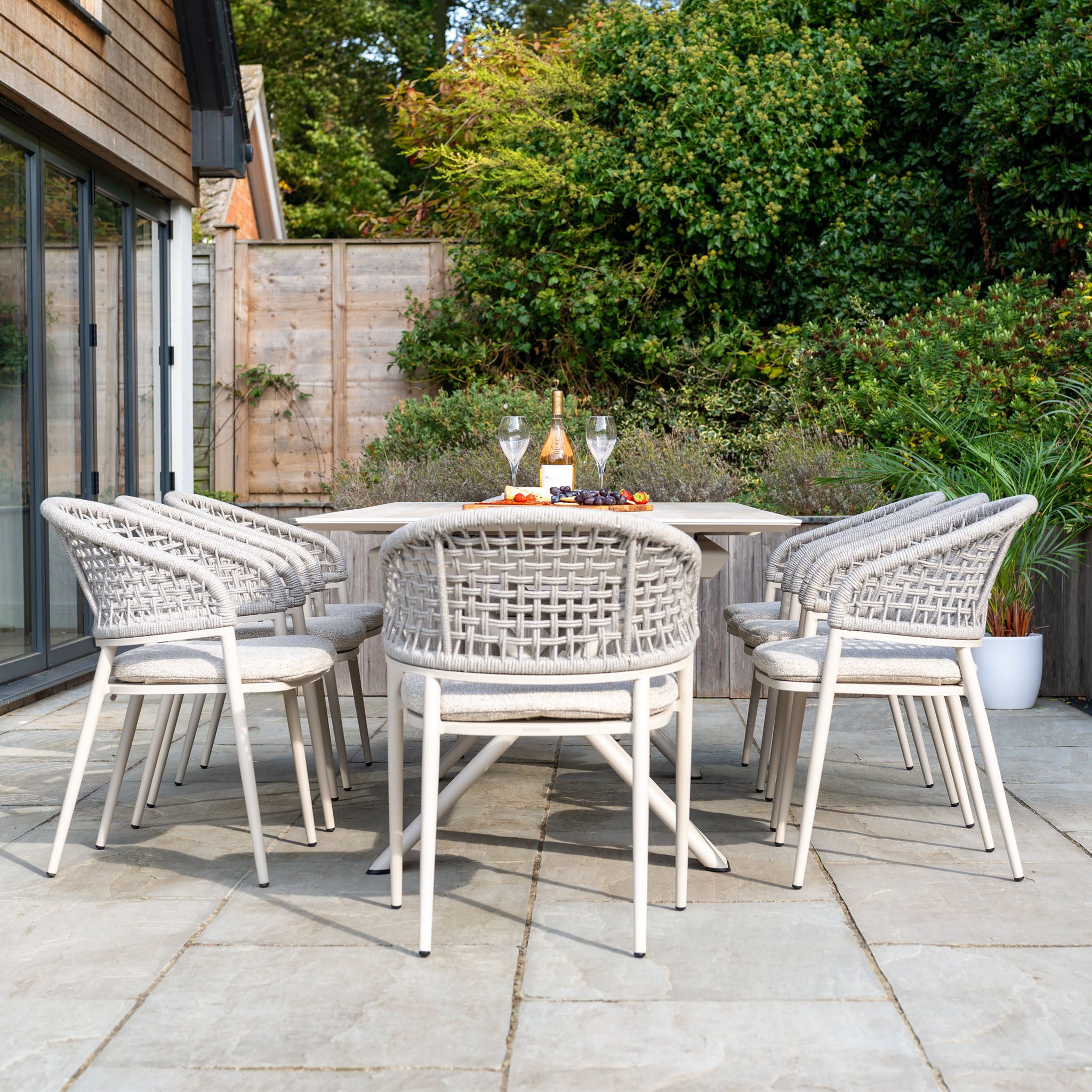 The Kalama 8 Seat Rope Dining Set with Albatross Extending Table in Oatmeal offers stylish outdoor dining, ideal for gathering with wine, glasses, and snacks on a tiled terrace.