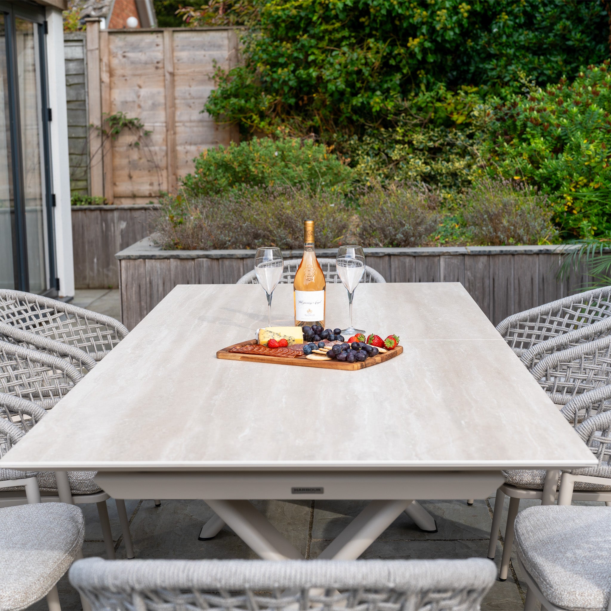 The Kalama 8 Seat Rope Dining Set with Albatross Extending Table in Oatmeal brings elegant outdoor dining to your garden, perfect for gatherings with wine, cheese, and friends.