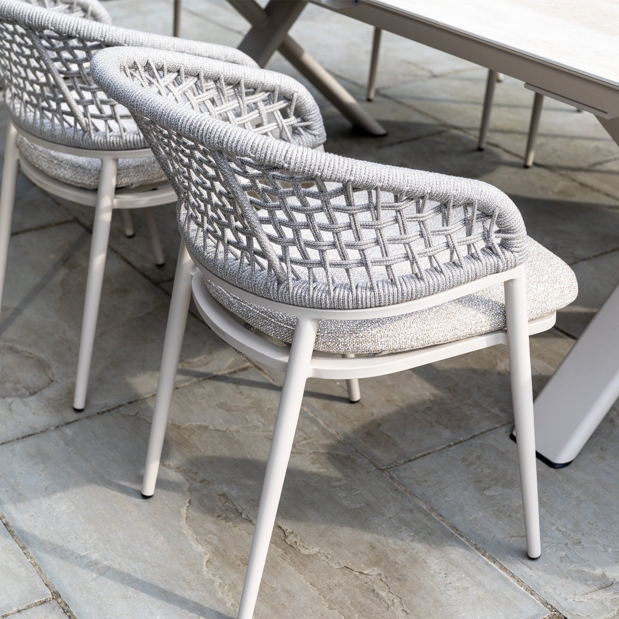 Two modern outdoor chairs from the Kalama 6 Seat Rope Dining Set with Albatross Extending Table in Oatmeal are arranged on a stone patio.