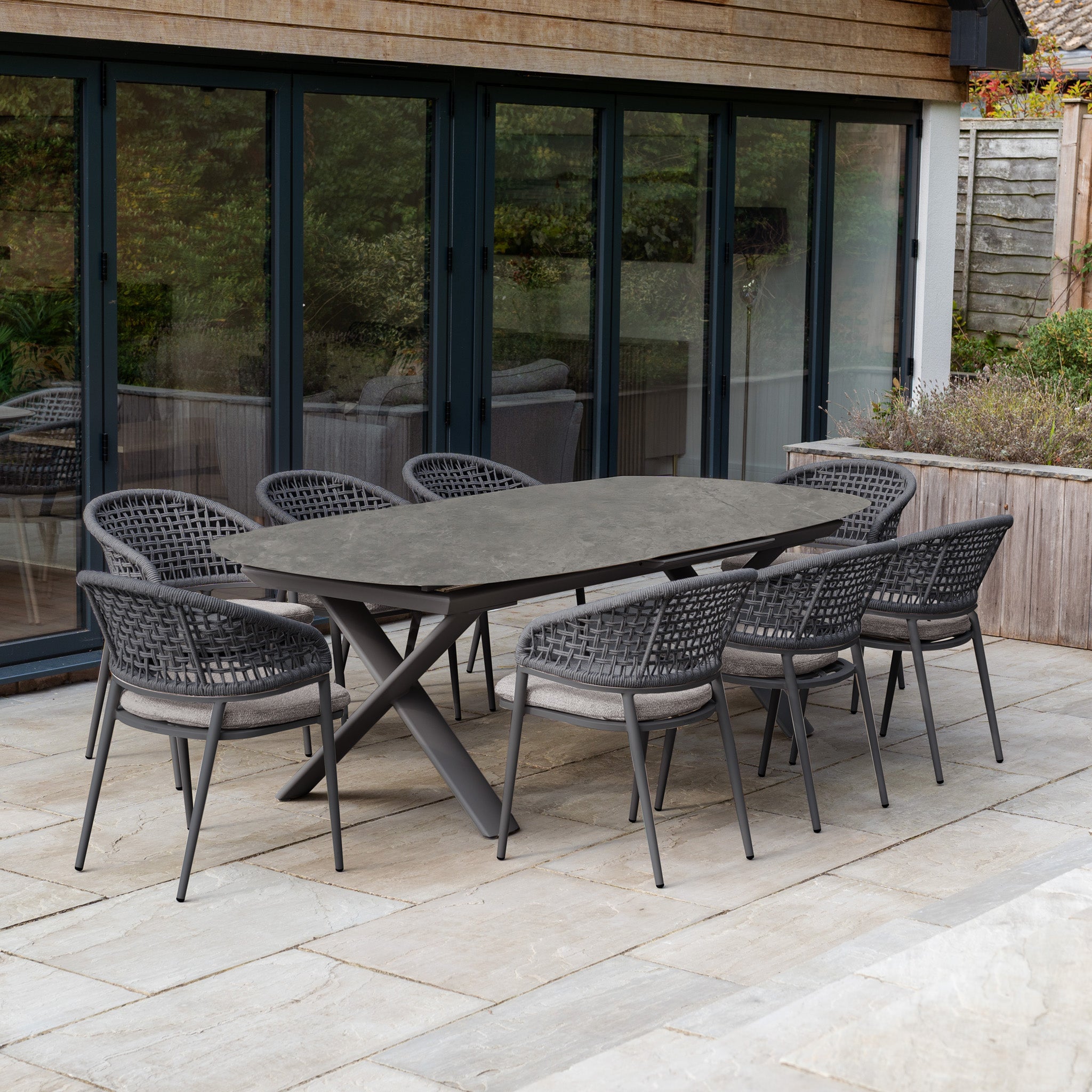 A stone patio by glass doors features the Kalama 8 Seat Oval Rope Dining Set with Albatross Extending Table in Truffle—an ideal choice for stylish outdoor dining furniture.