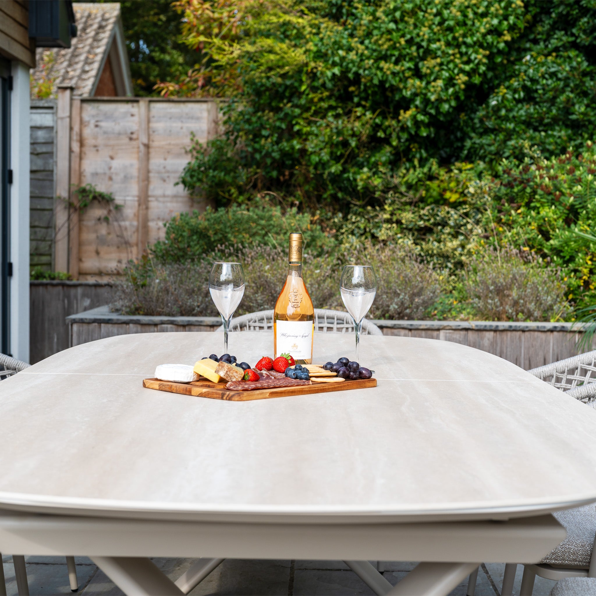 An outdoor table set with wine, two glasses, cheese, and fruit on a wooden board sets the perfect scene for enjoying the Kalama 8 Seat Oval Rope Dining Set with Albatross Extending Table in Oatmeal.