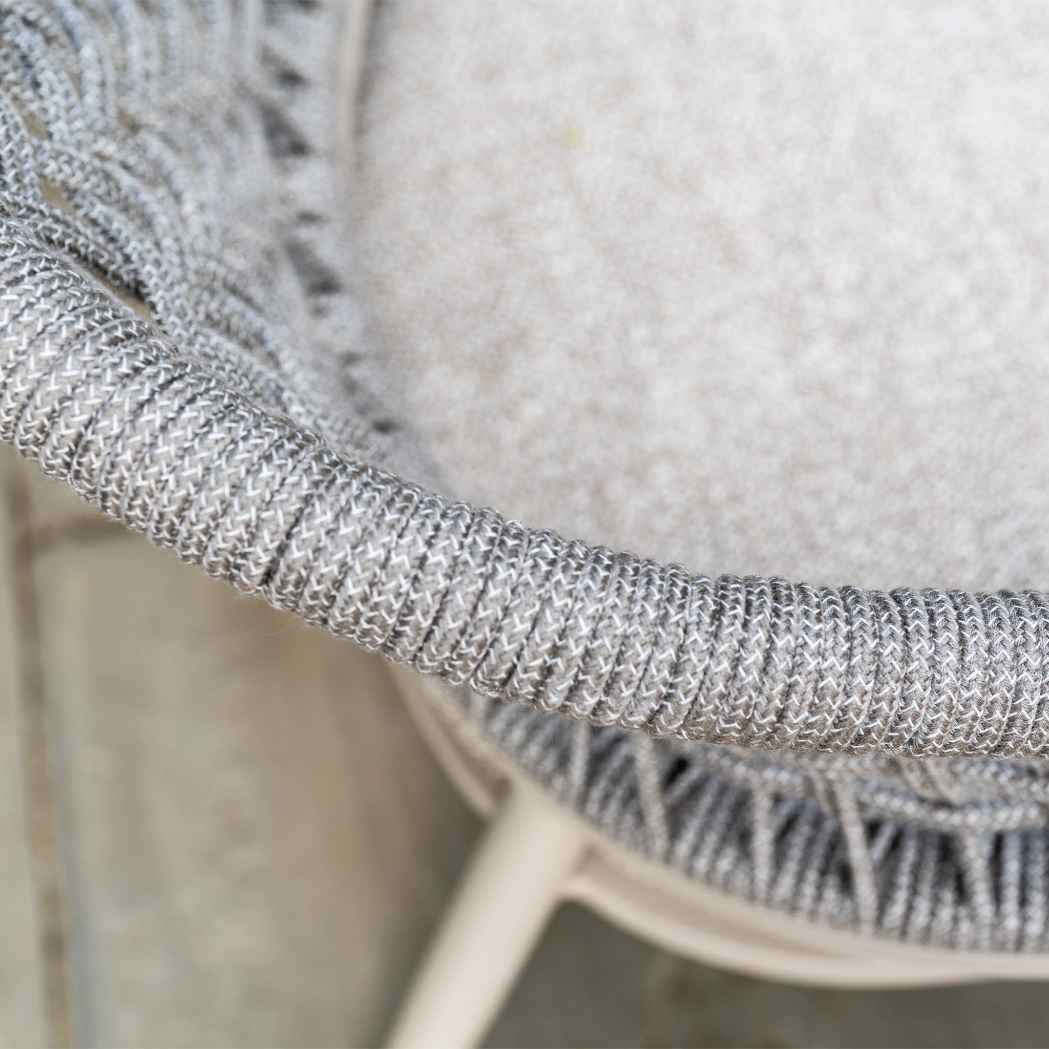 Close-up of a woven gray chair with a textured cushion, part of the Kalama 8 Seat Oval Rope Dining Set with Albatross Extending Table in Oatmeal, shown on a light-colored floor.