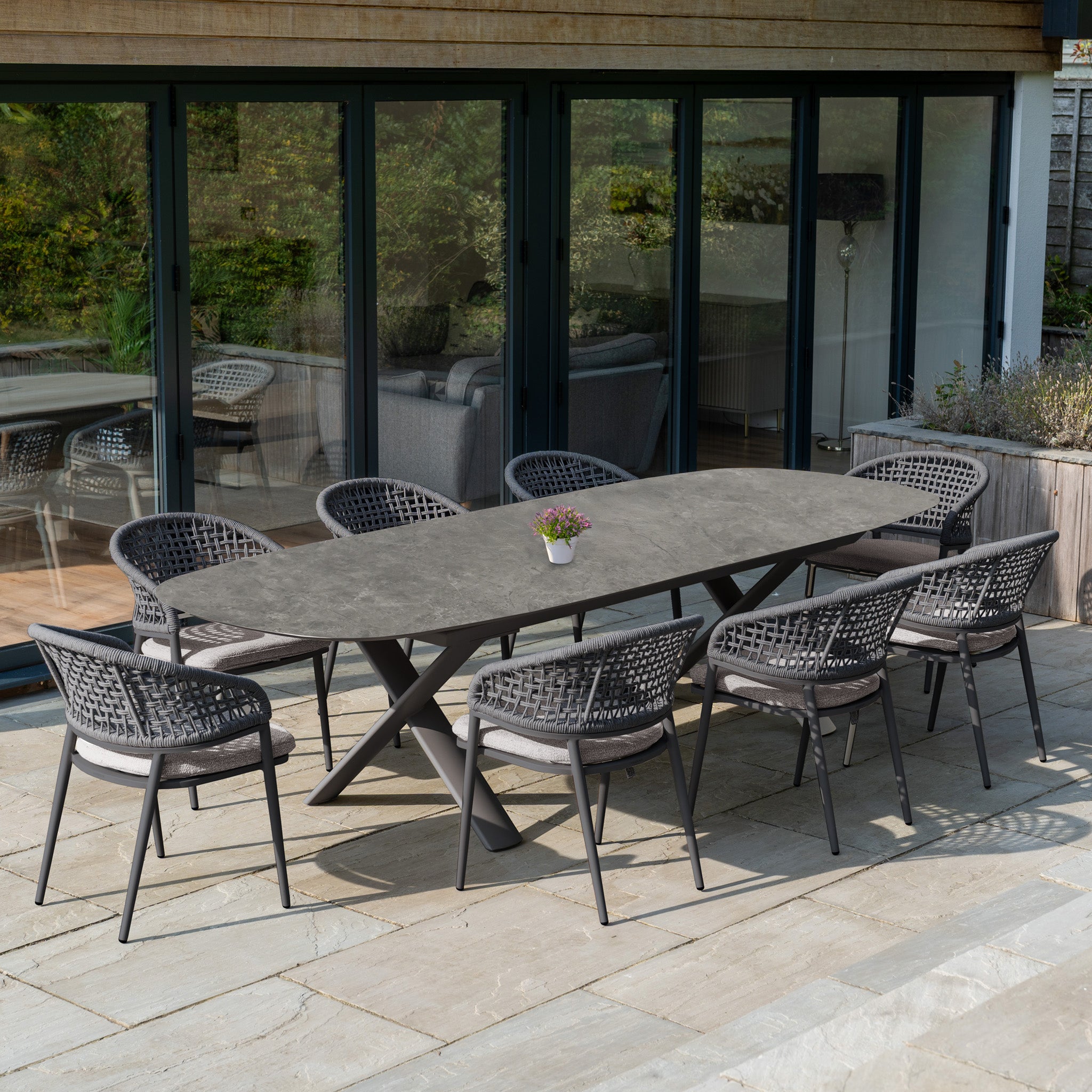 Modern outdoor patio featuring the Kalama 8 Seat Oval Rope Dining Set with Albatross Extending Table in Truffle, eight chairs, and a potted plant centerpiece—perfect for stylish outdoor dining.