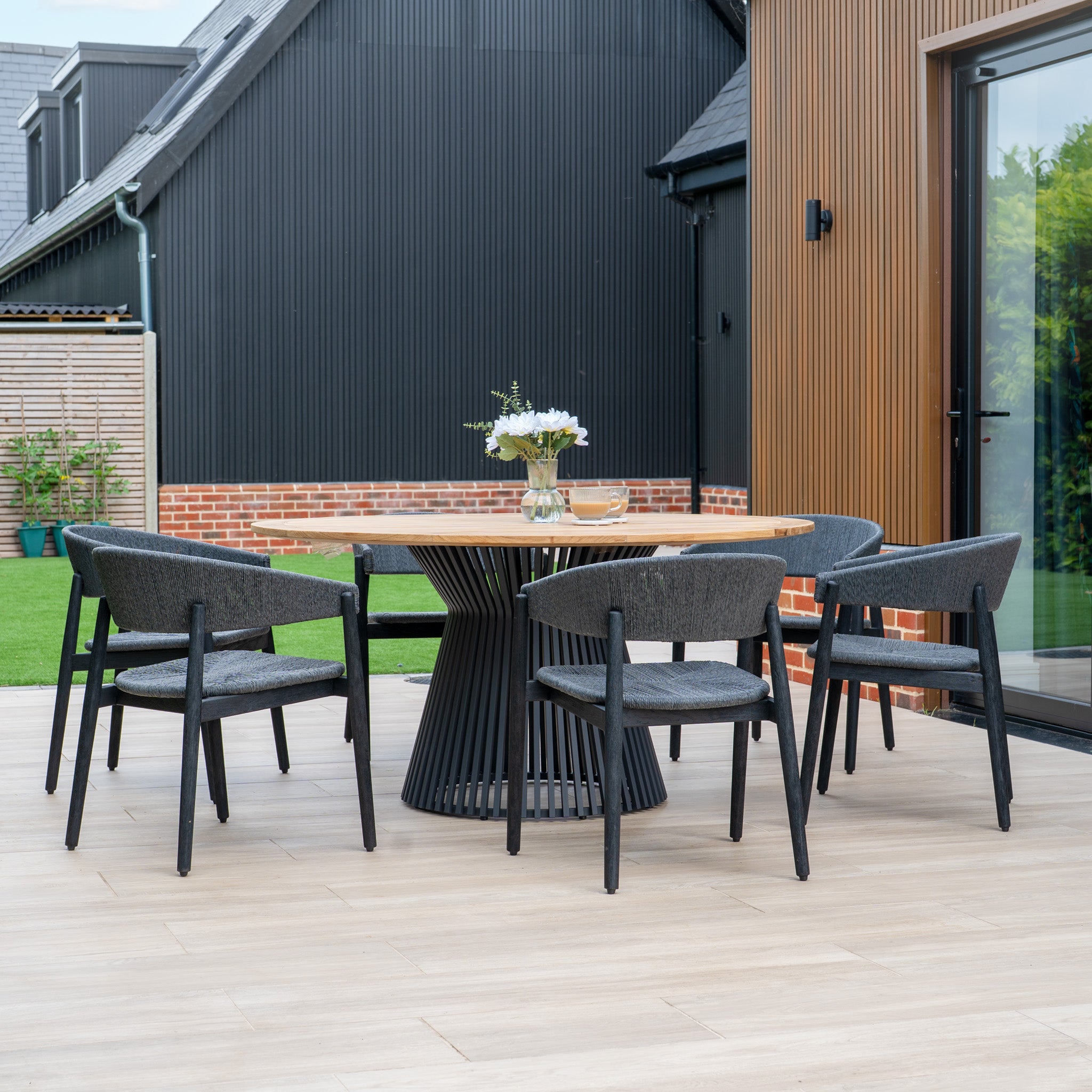 Create a stylish outdoor space with the Lucca 6 Seat Dining Set, featuring a round teak table and six black chairs—ideal for modern patio gatherings.